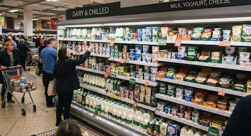 Shoppers browsing a grocery dairy aisle with refrigerated milk and cheese displays