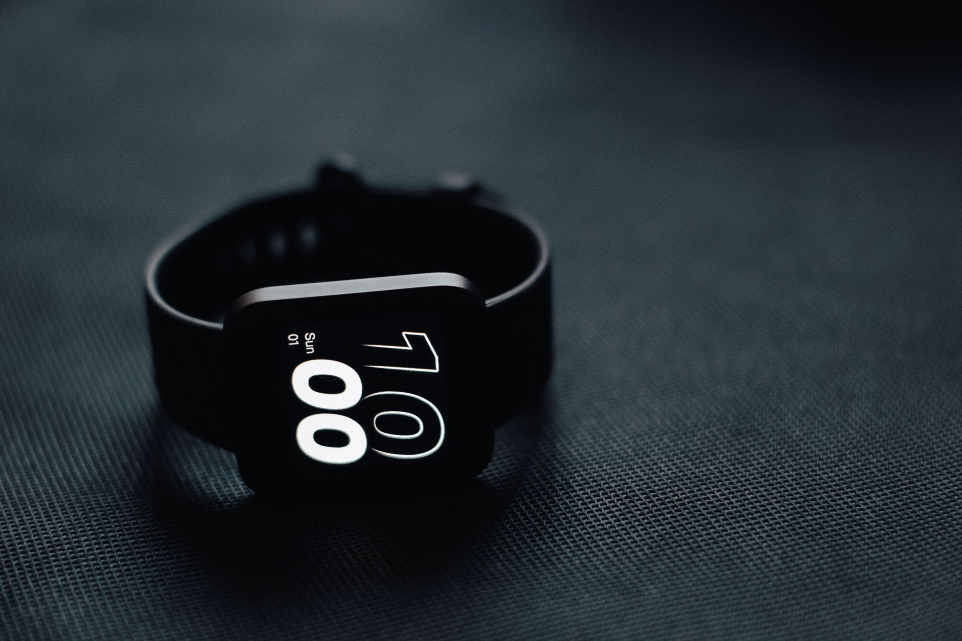 Black smartwatch on a dark surface, displaying 10:00 on the screen.