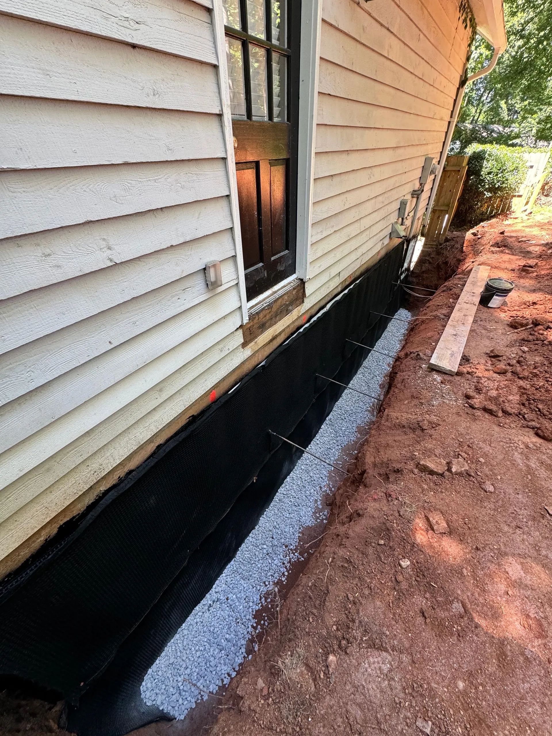 House exterior with black waterproofing along the foundation and gravel border beside dirt trench