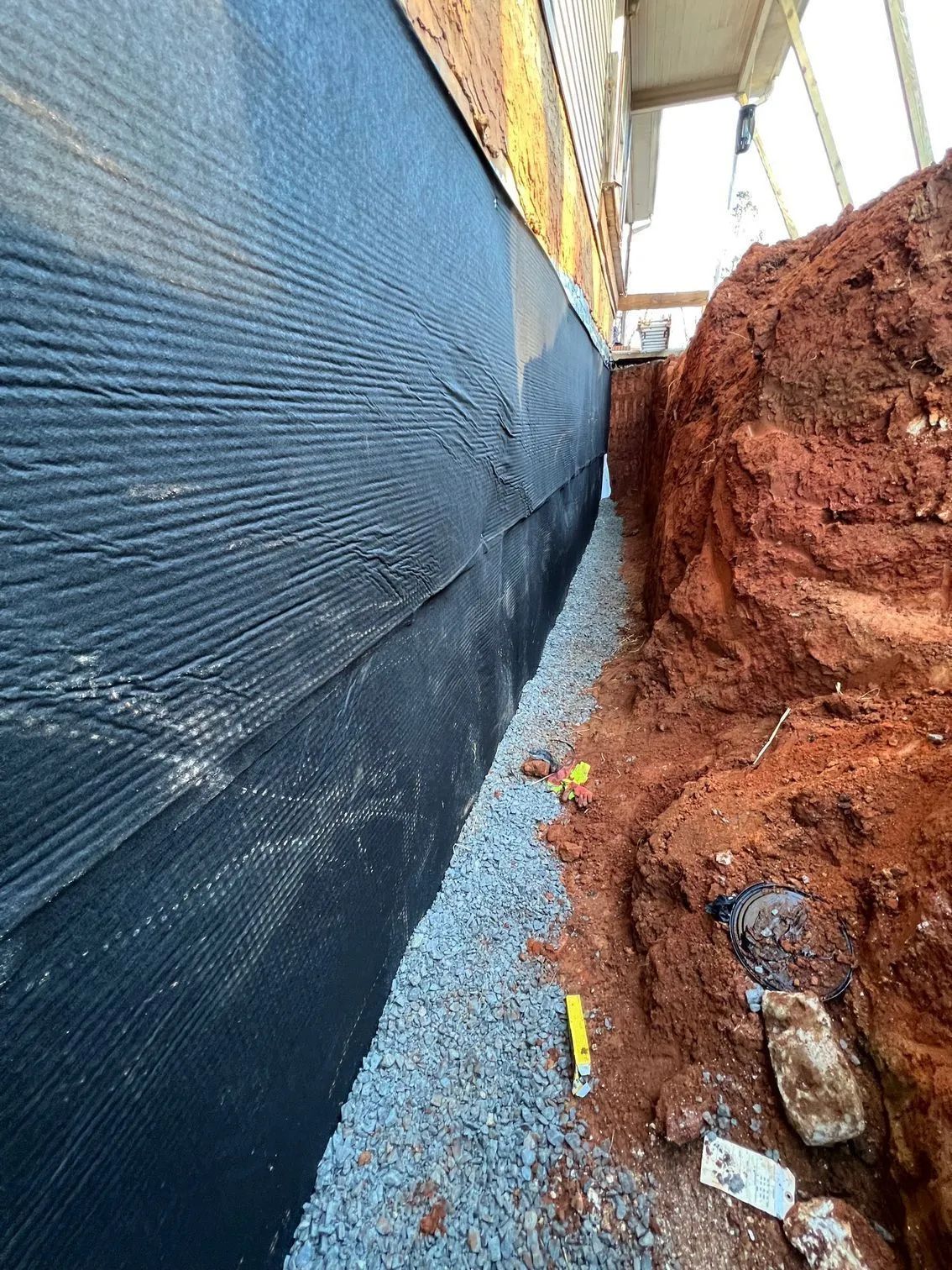 Foundation wall with black drainage membrane, gravel, and excavated soil.
