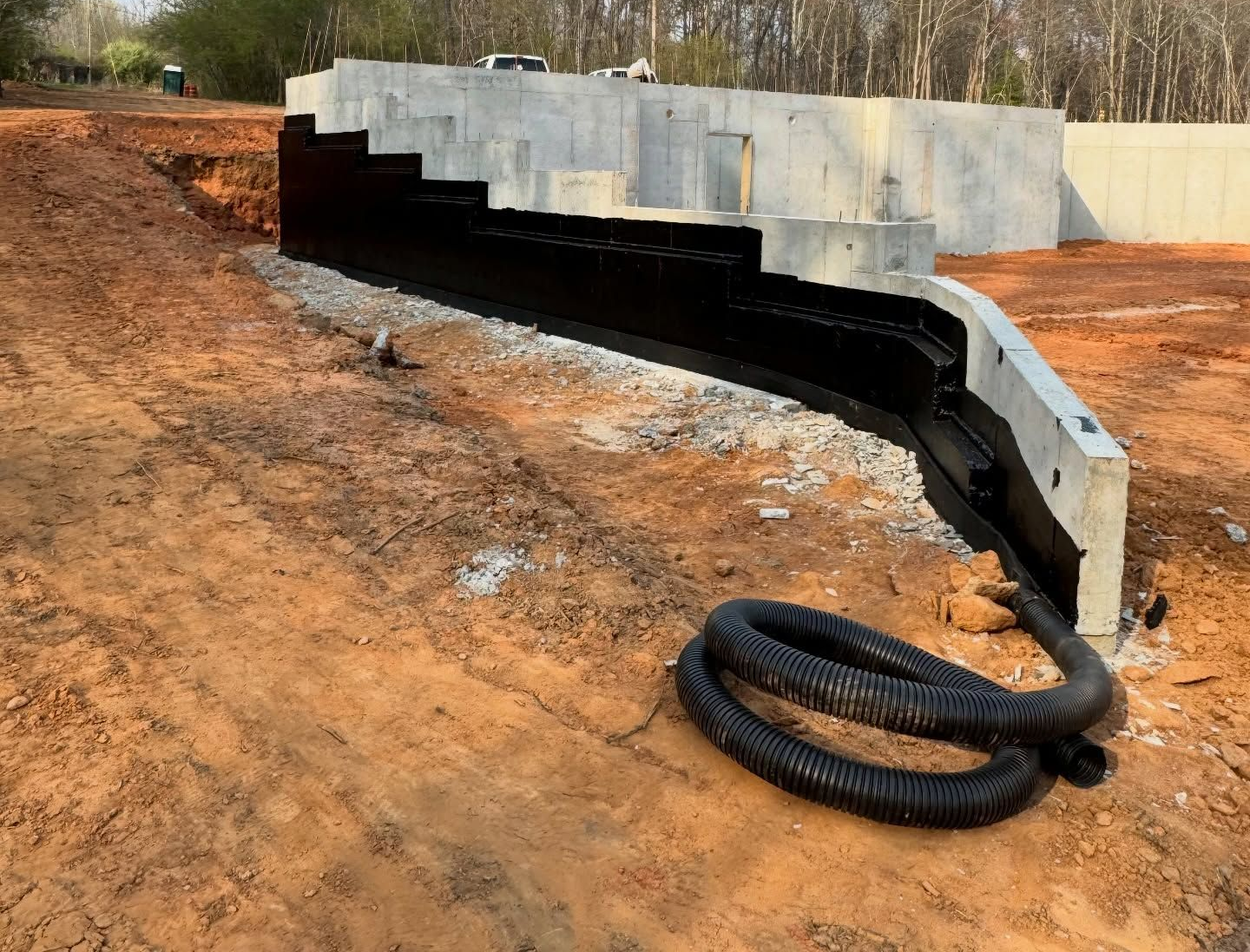 Black drainage pipe on a dirt slope beside a concrete retaining wall, with coiled hose in foreground.