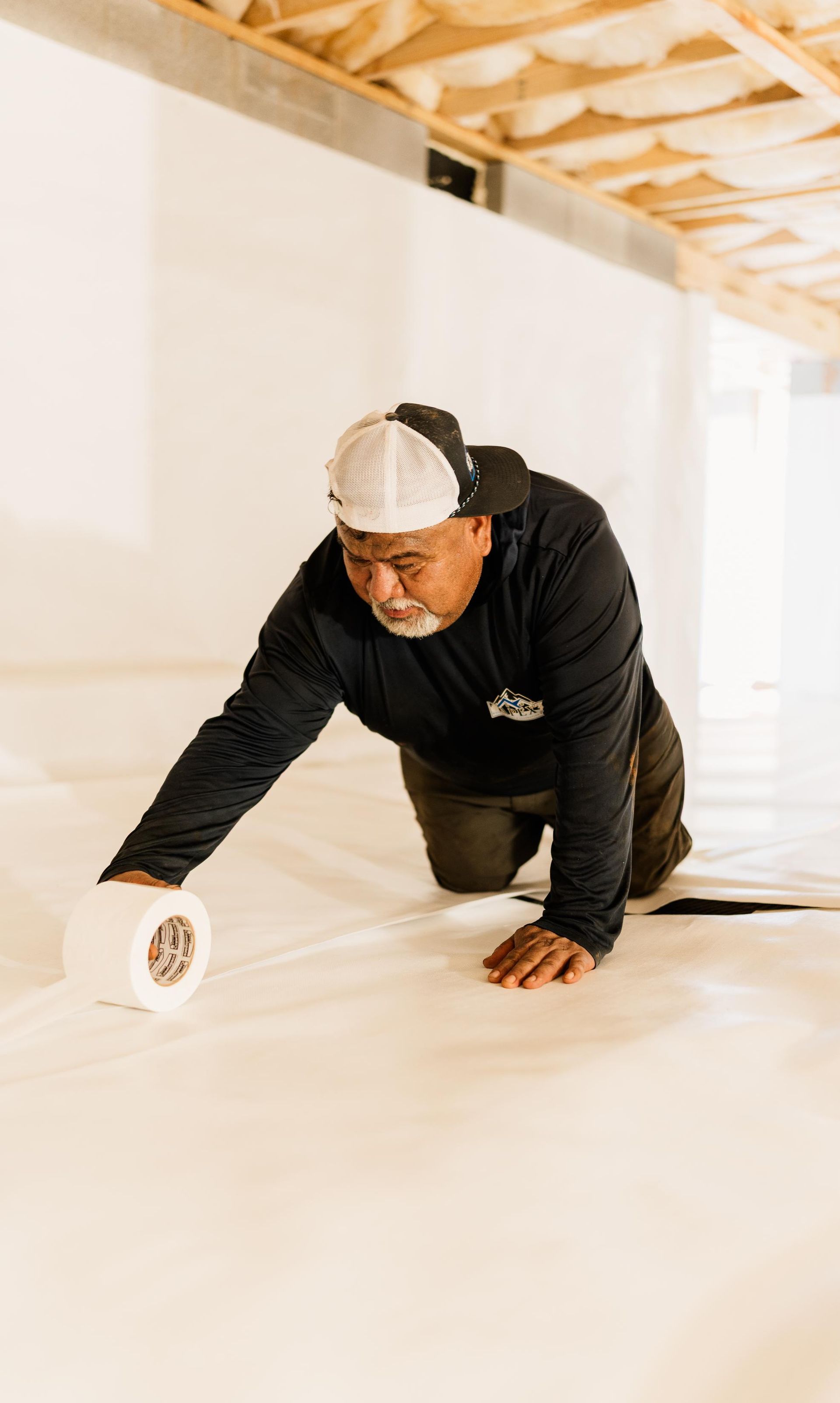 Worker kneeling on a floor, unrolling white material inside a room under construction