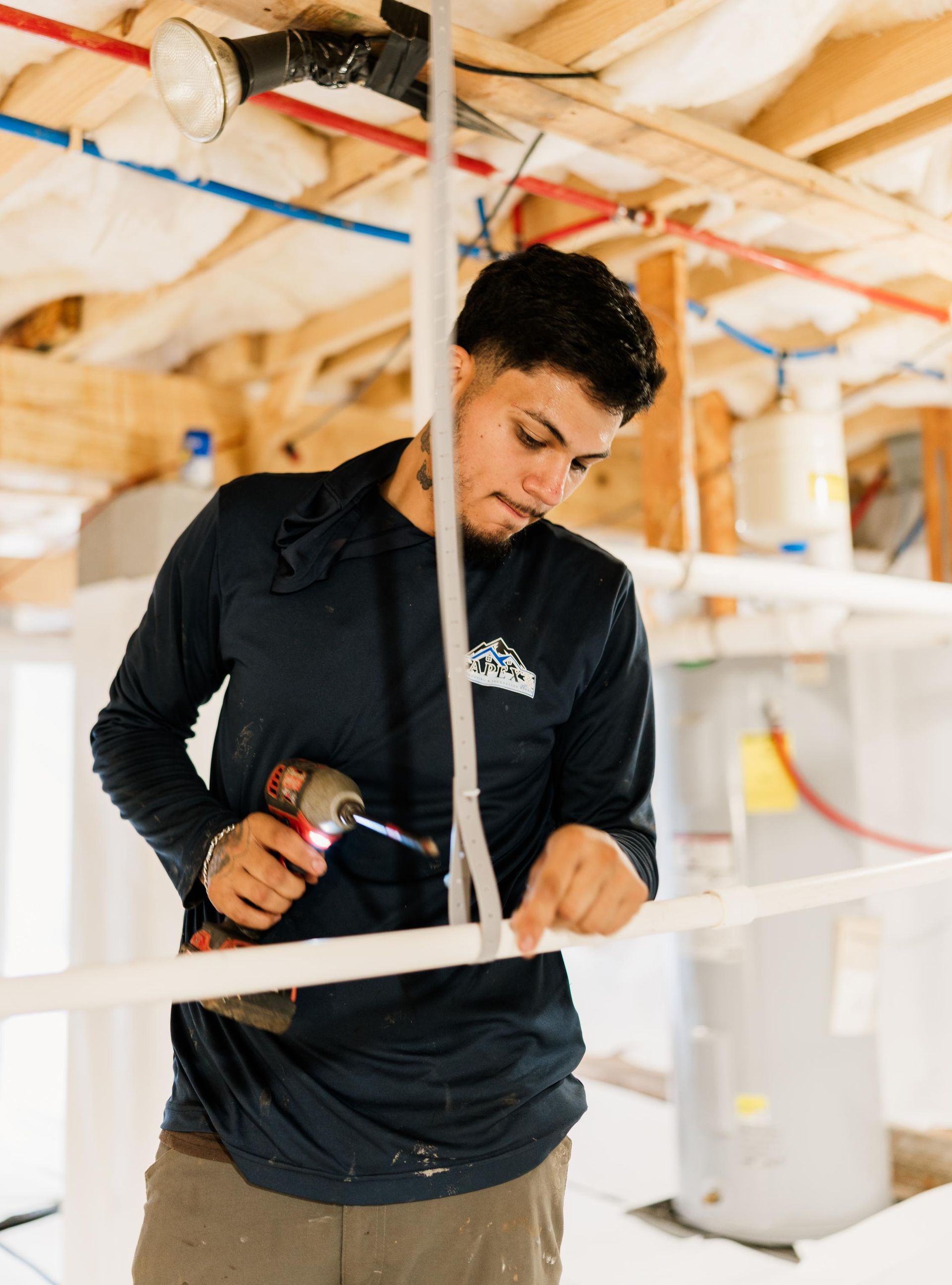 Worker using a power drill in an unfinished interior with exposed wiring and framing