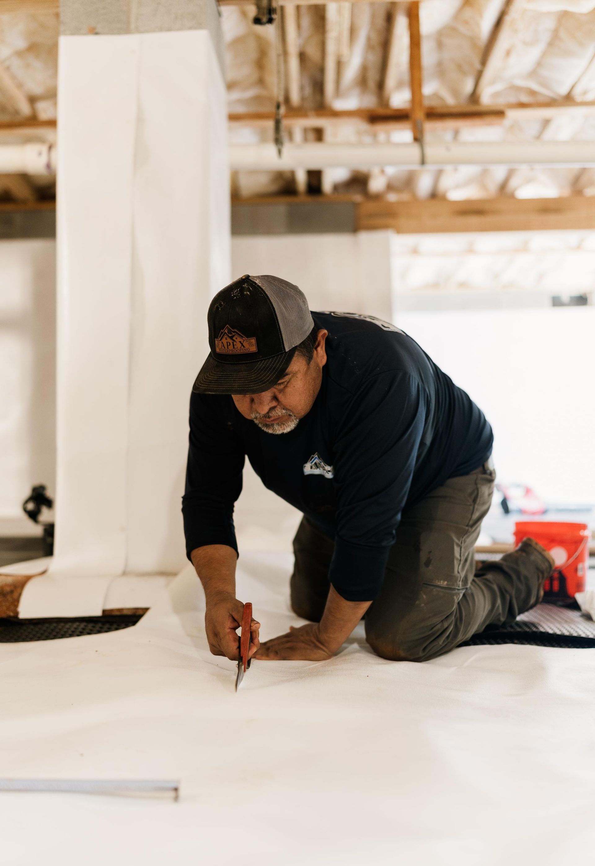 Worker kneeling on a floor, marking white sheeting in a construction site.