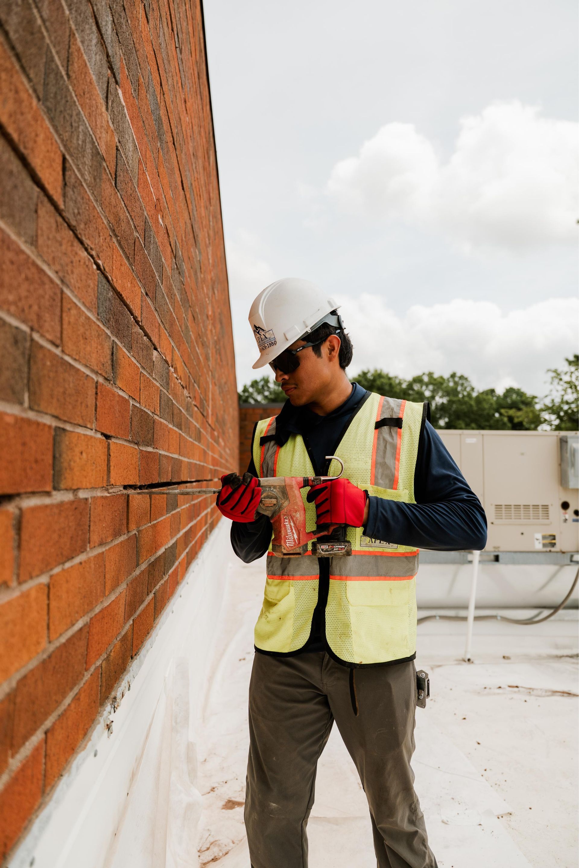 Construction worker marking measurements on a brick wall with a tape measure at an outdoor site