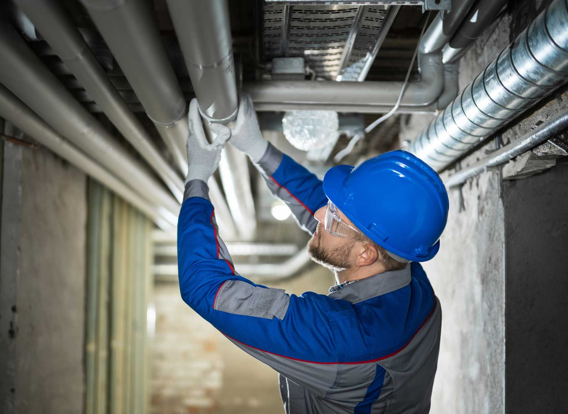 Worker inspecting water pipes for leaks in basement.