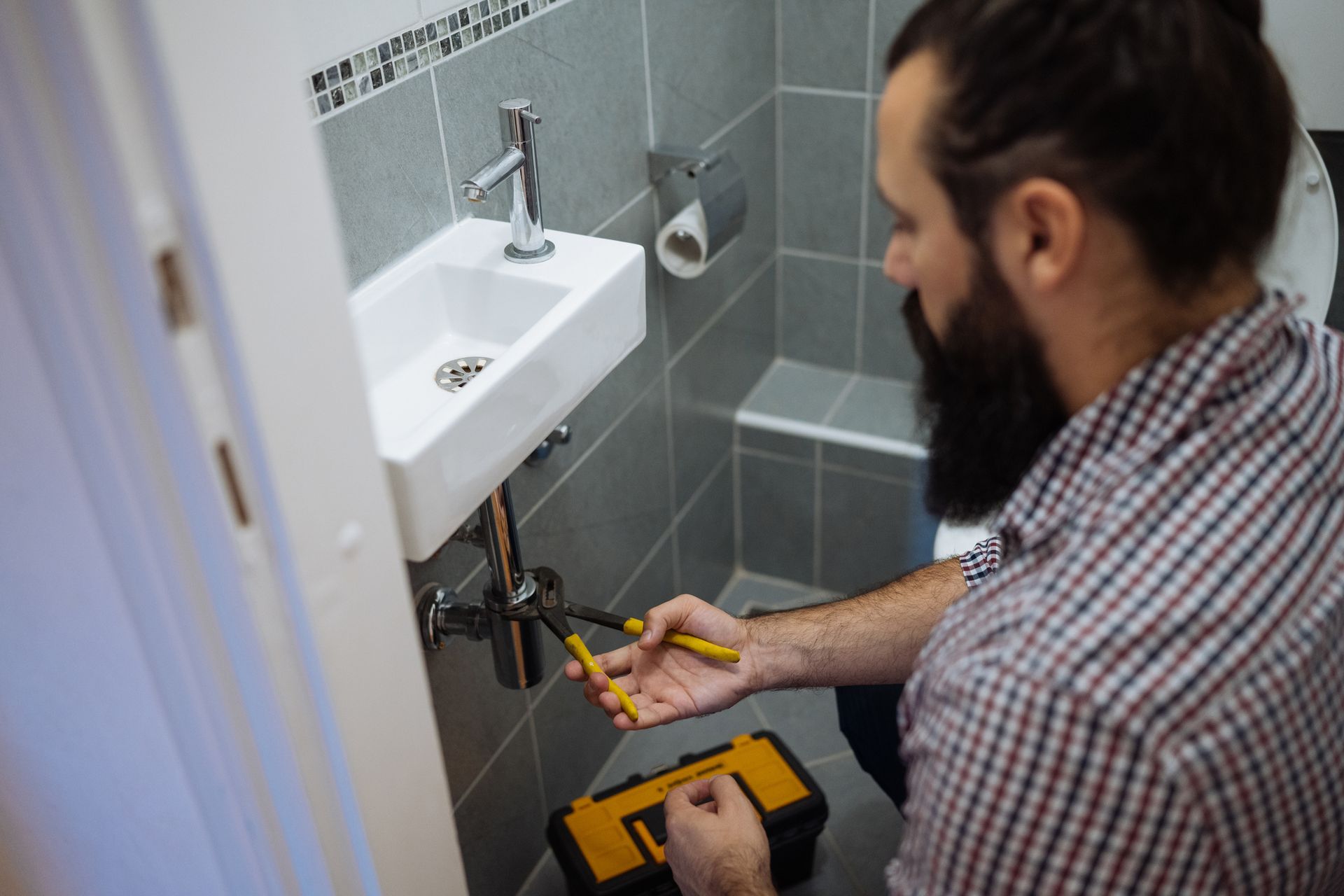 A plumber fixing under a bathroom sink at a customer’s home.