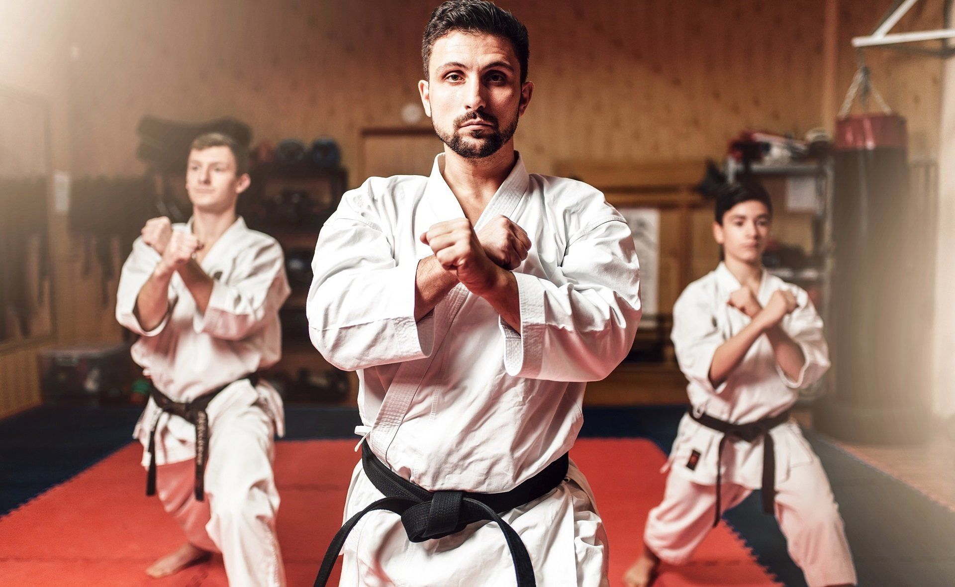 Karate practitioners in white gis with black belts, in a training hall, in fighting stance.