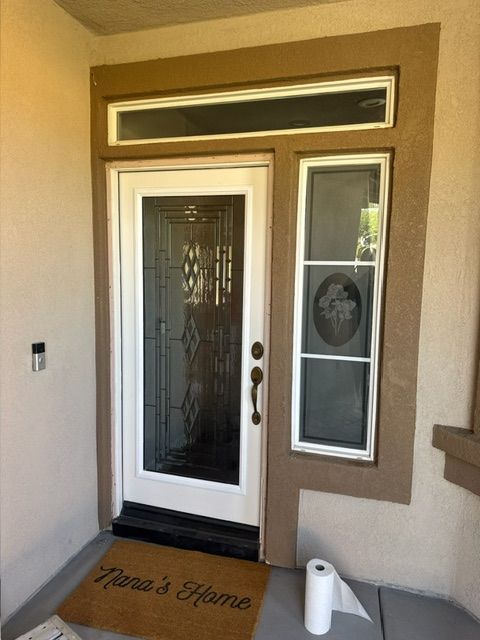 Exterior view of a home's entryway with a white door, windows, and brown trim. A welcome mat says