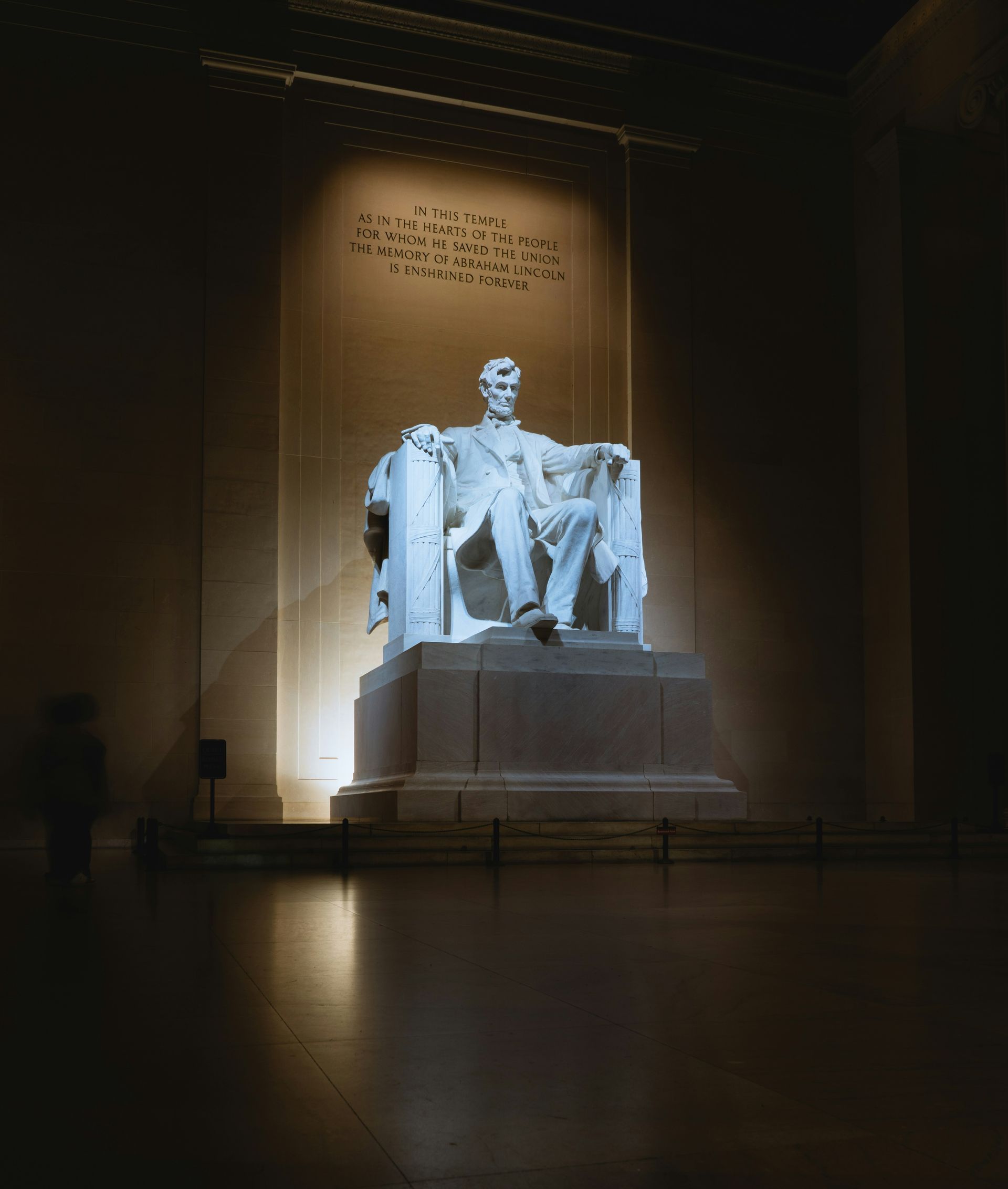 Lincoln Memorial statue illuminated in a dim hall, with inscription above and a dark reflective floor