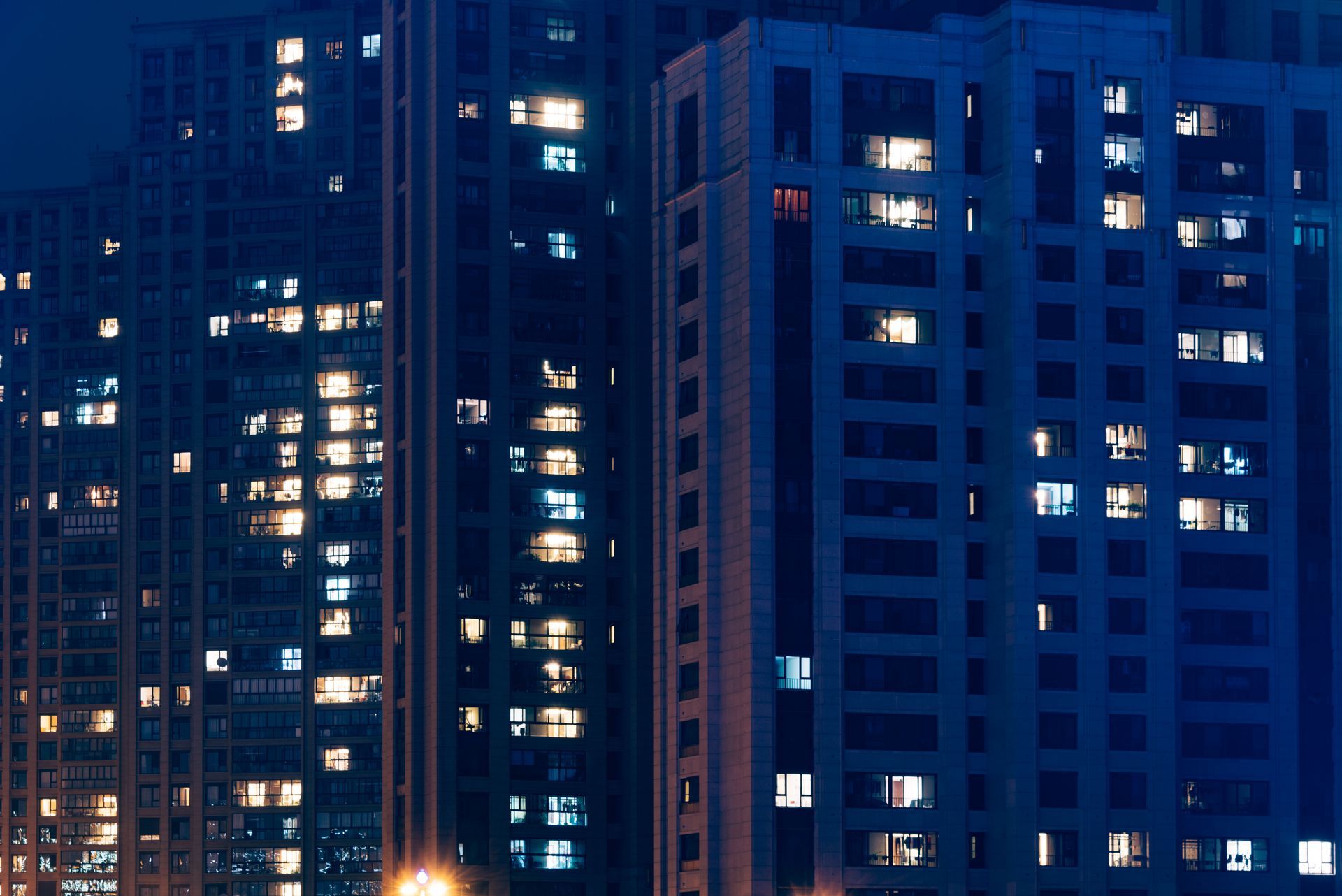 Nighttime view of tall apartment buildings with many lit windows in blue-toned cityscape