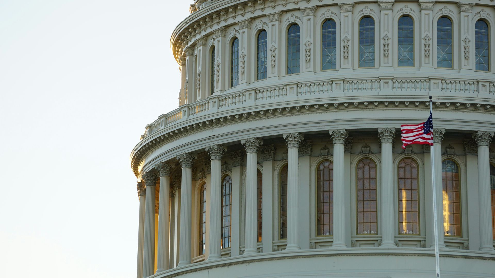 U.S. Capitol dome with columns and a waving American flag at dusk