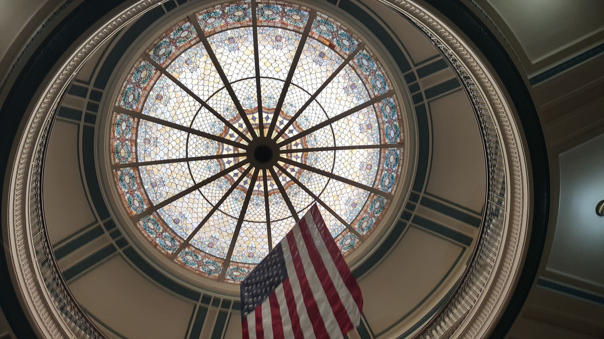 Dome ceiling with ornate stained glass and a hanging American flag below