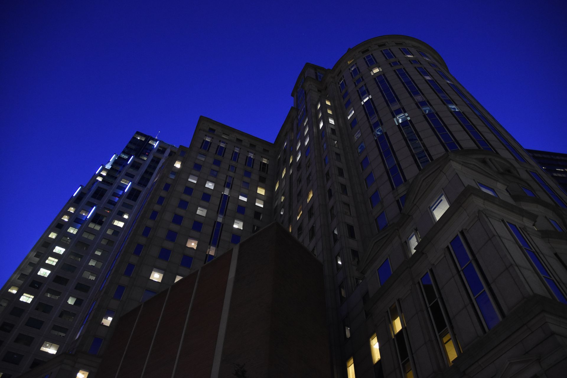 Low-angle view of tall city buildings at night, lit by blue lights against a dark sky