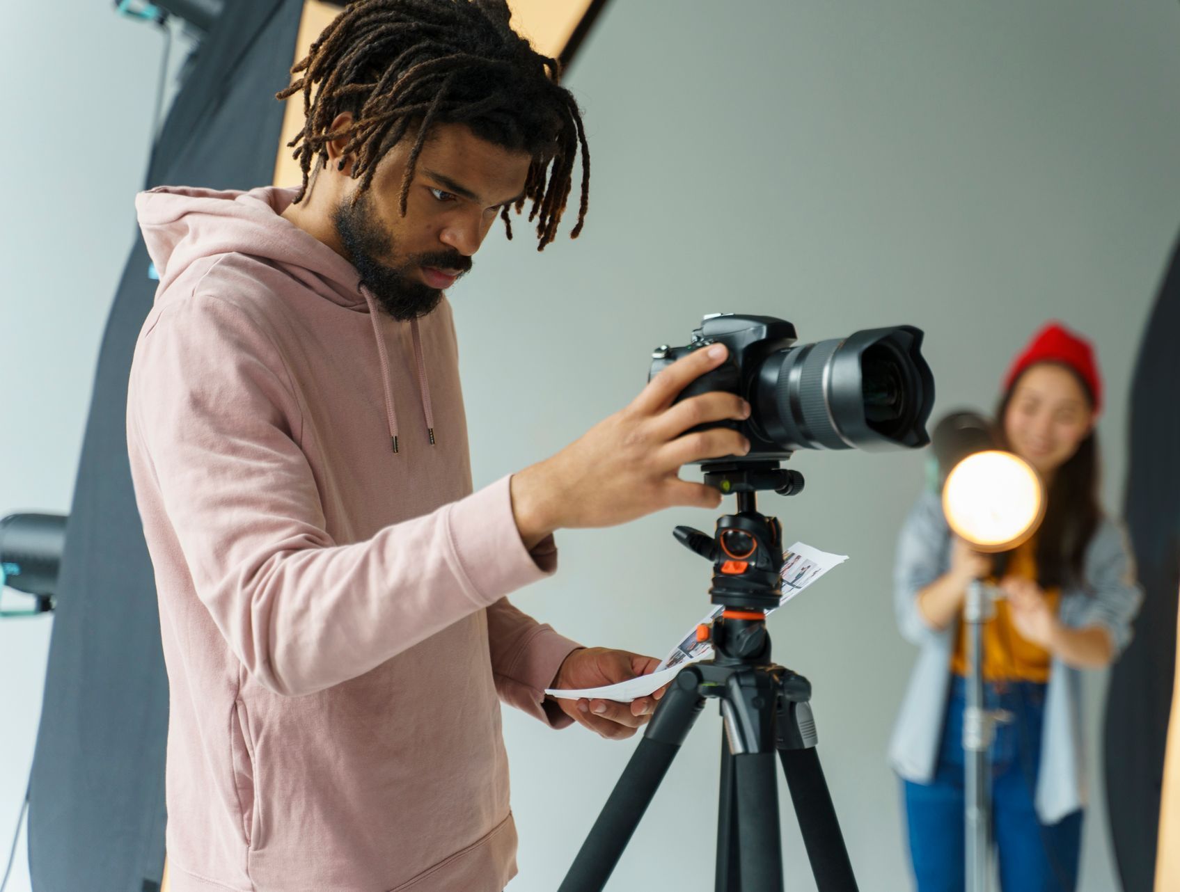 Photographer adjusting a camera on a tripod while a model poses in a studio with lights.