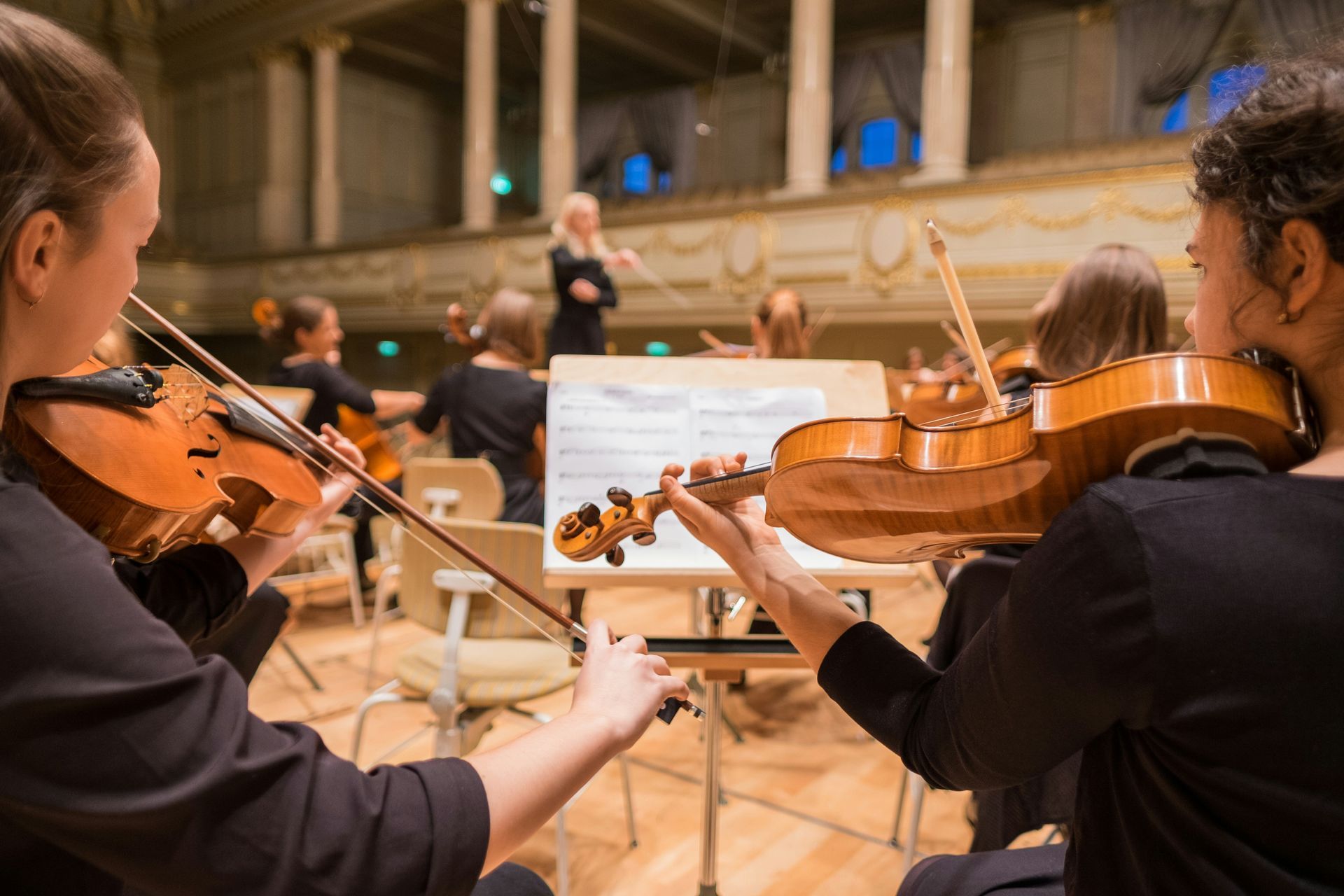 Orchestra musicians playing violins during a rehearsal in a concert hall