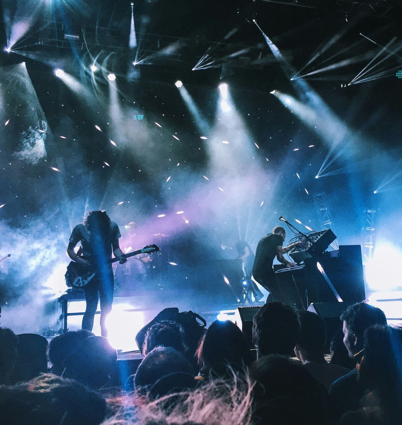 Concert stage with blue-white spotlights, silhouetted musicians, and cheering crowd in the foreground