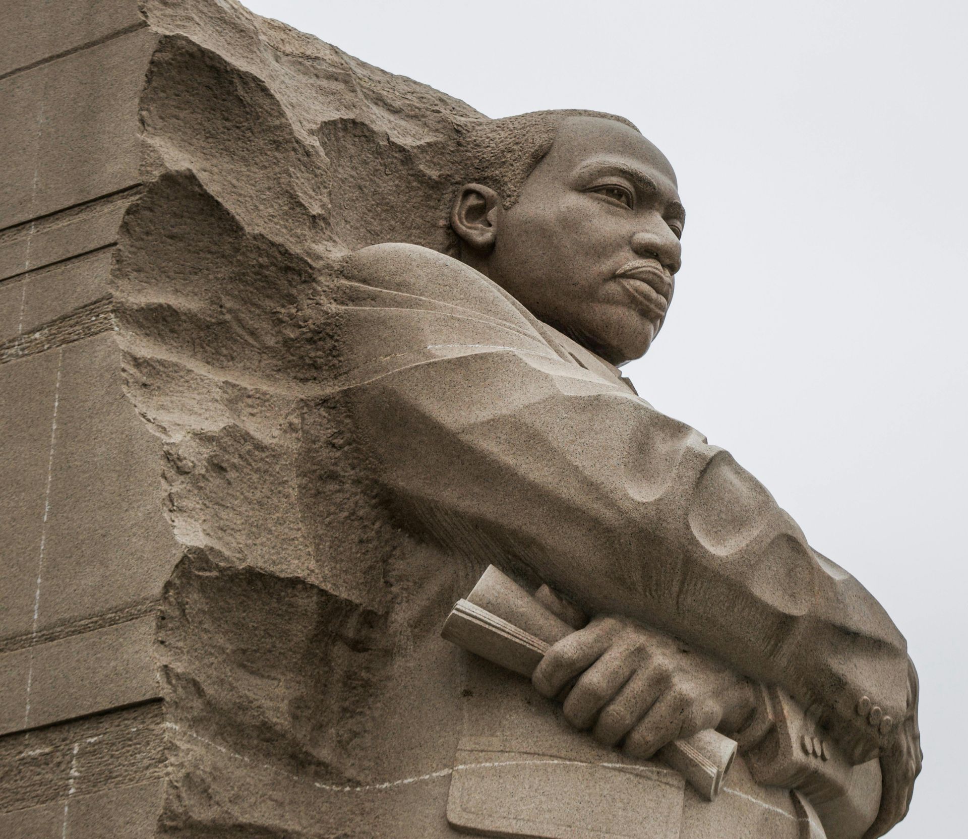 Stone statue of a man holding a book, carved in relief against a cloudy sky