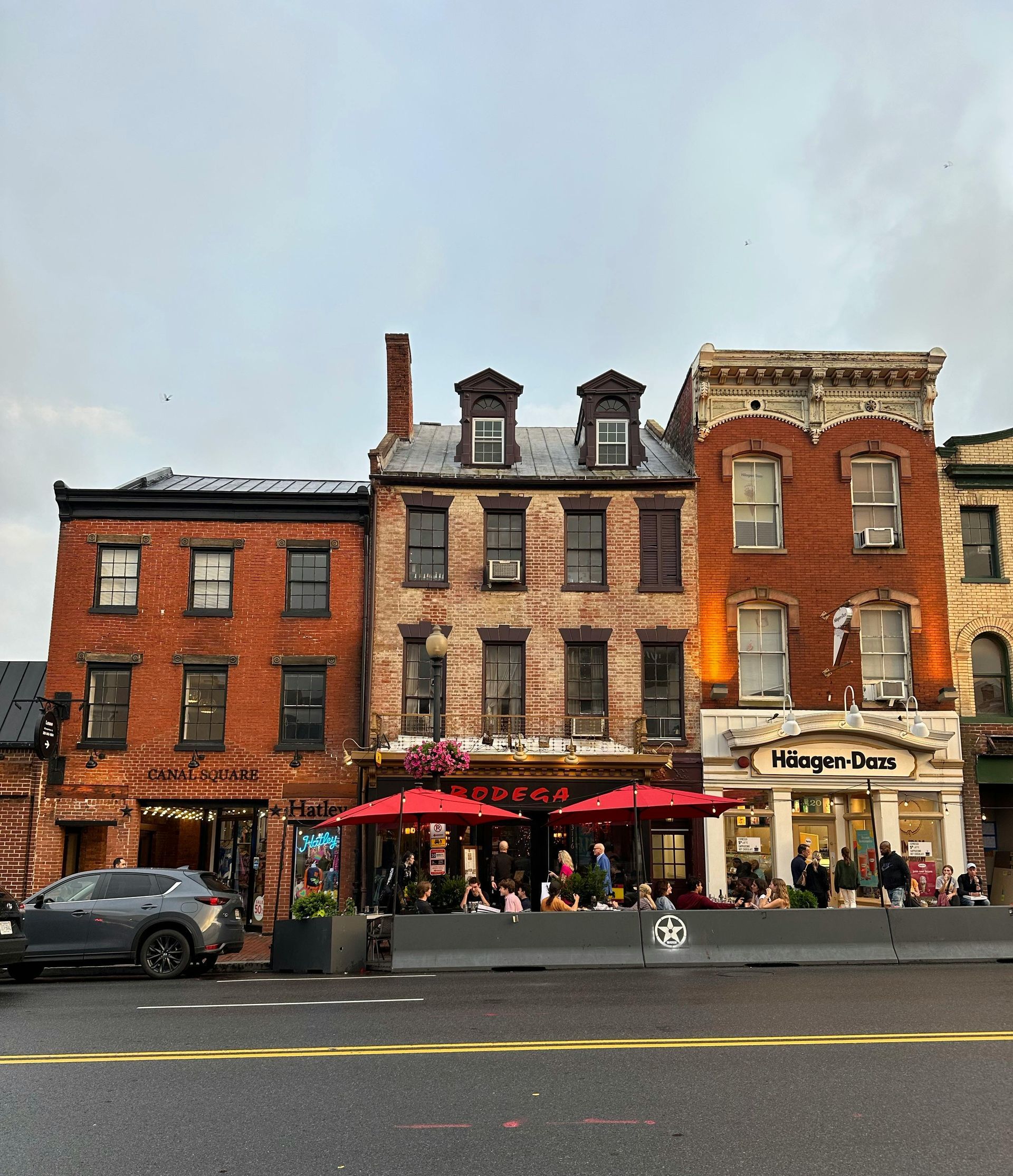 Row of red-brick storefronts with outdoor seating on a rainy street