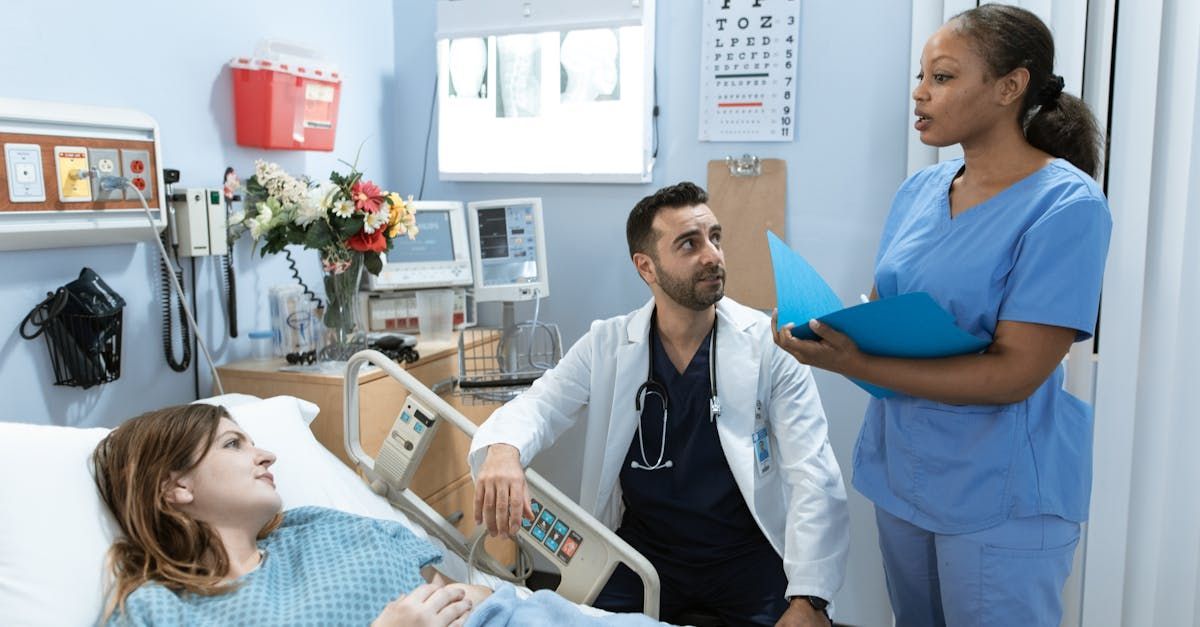 Hospital room with a patient in bed, a doctor, and a nurse discussing care by the bedside.