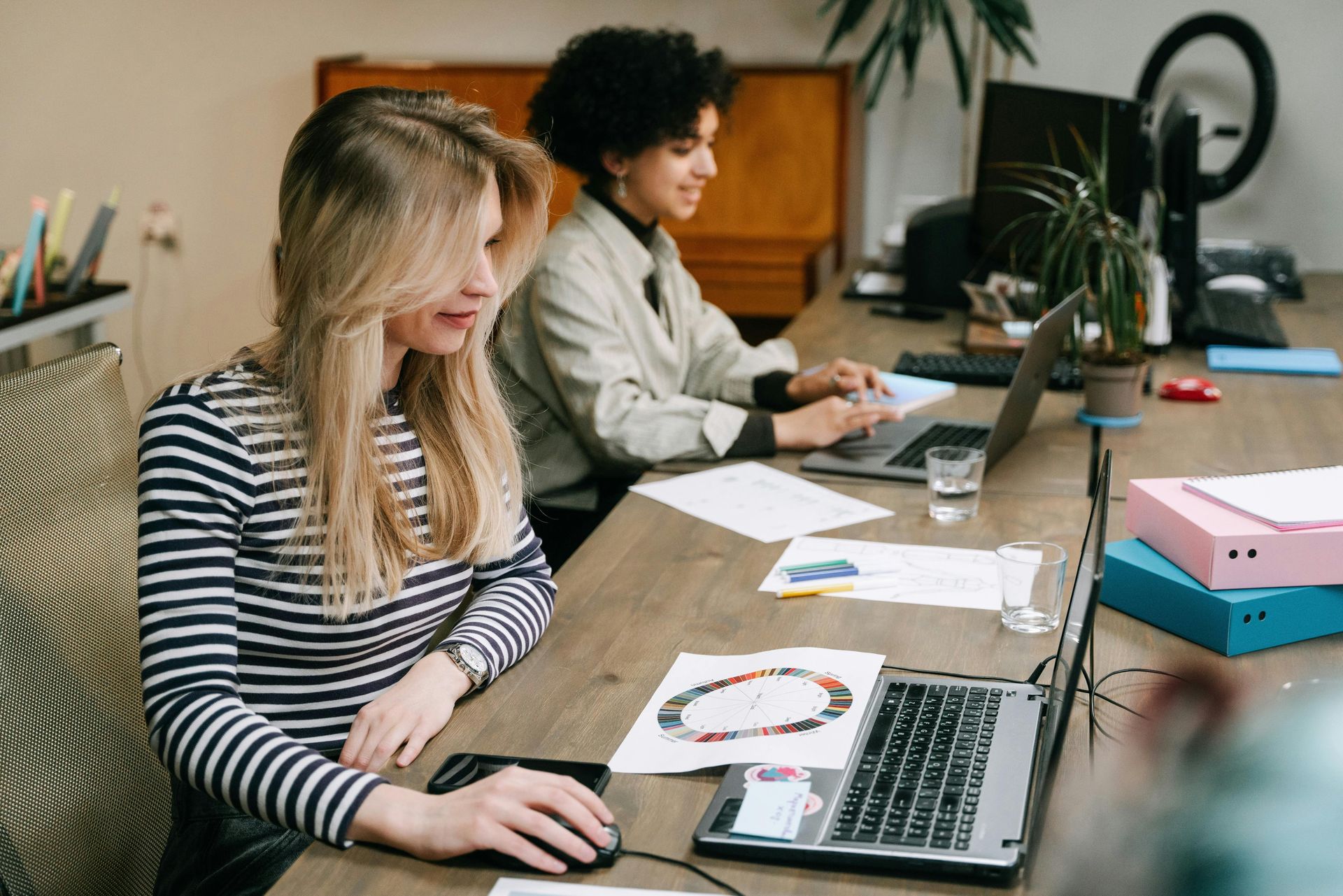 Two people working at a desk with laptops and papers in a bright office