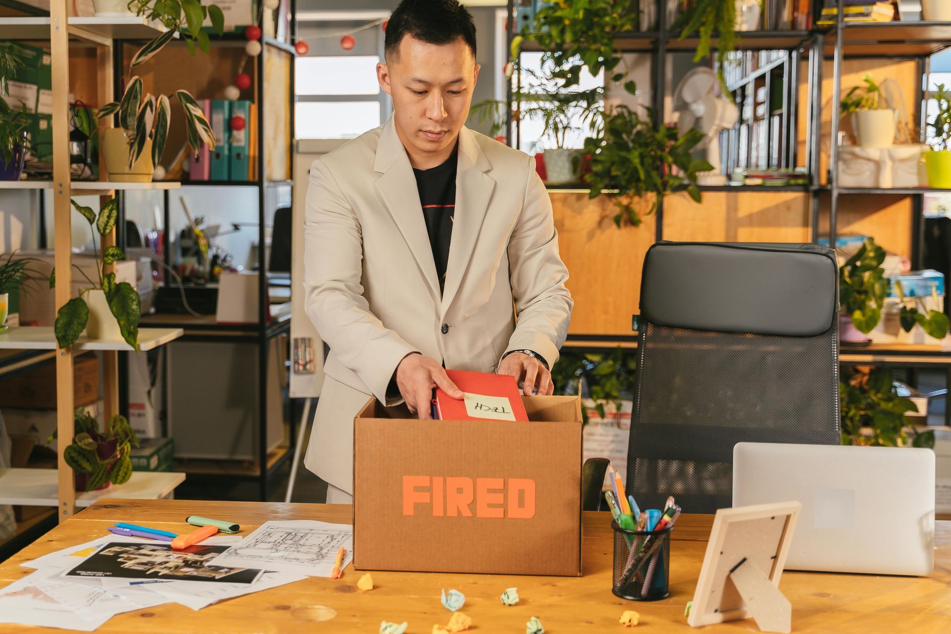 Man placing a red “FIRED” box on a desk in a modern office