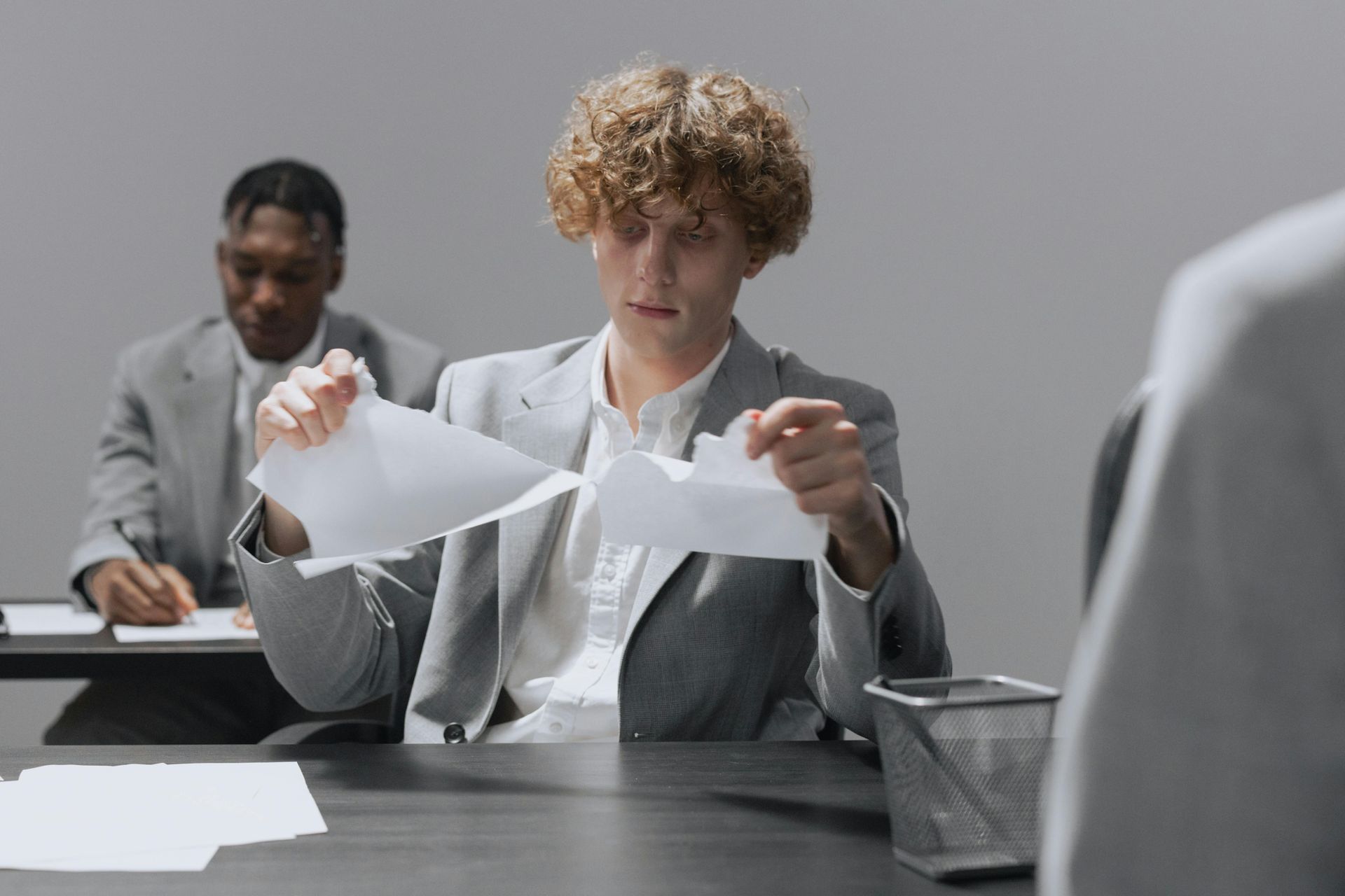 Person in a gray suit tearing a sheet of paper at a desk in a meeting room