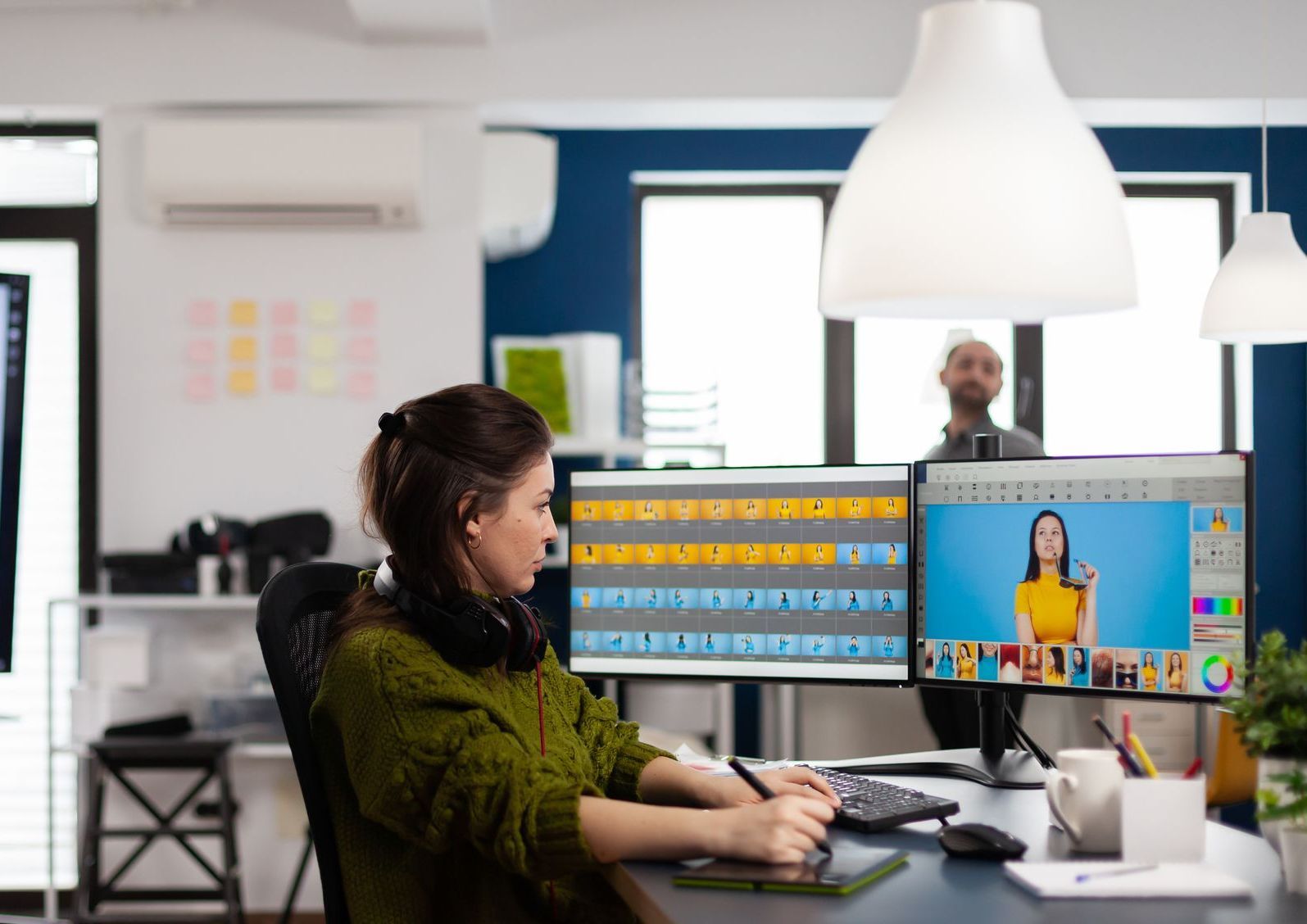 Person working at a desk with dual monitors in a bright office, video call visible on screen.
