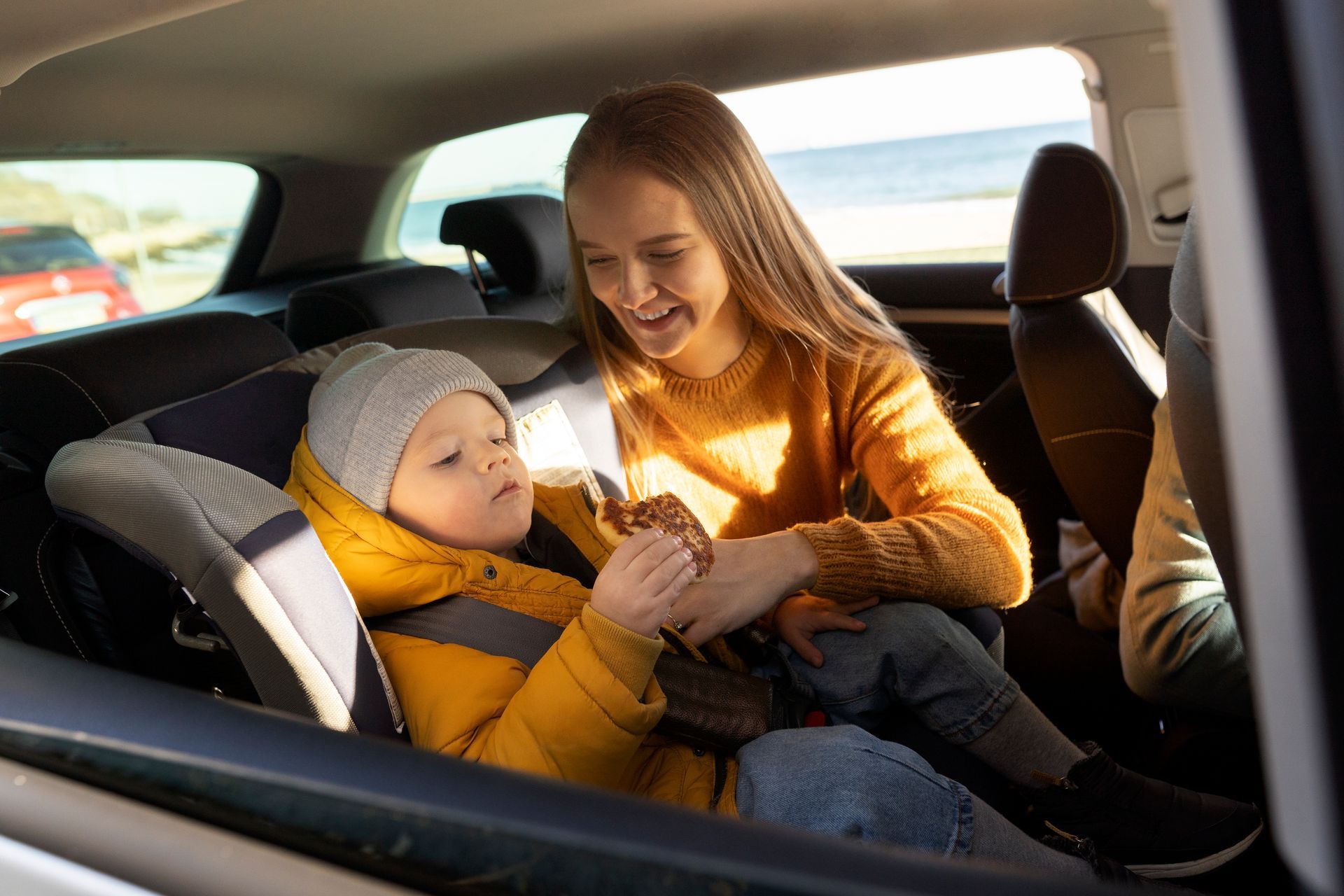 Woman buckles a child in a car seat in the back of a vehicle, both wearing yellow sweaters.