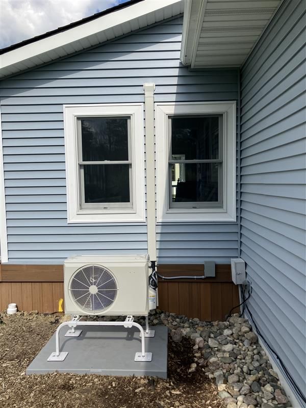 HVAC unit outside blue siding building with two windows. White support structure, on gravel and concrete base.