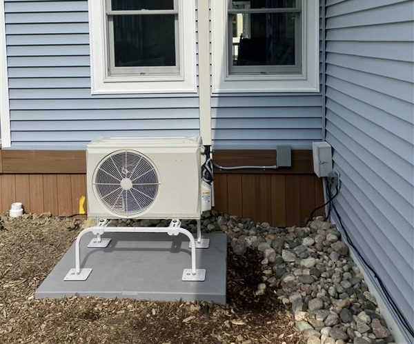 Outdoor air conditioning unit mounted on a concrete pad next to a blue house with rock landscaping.
