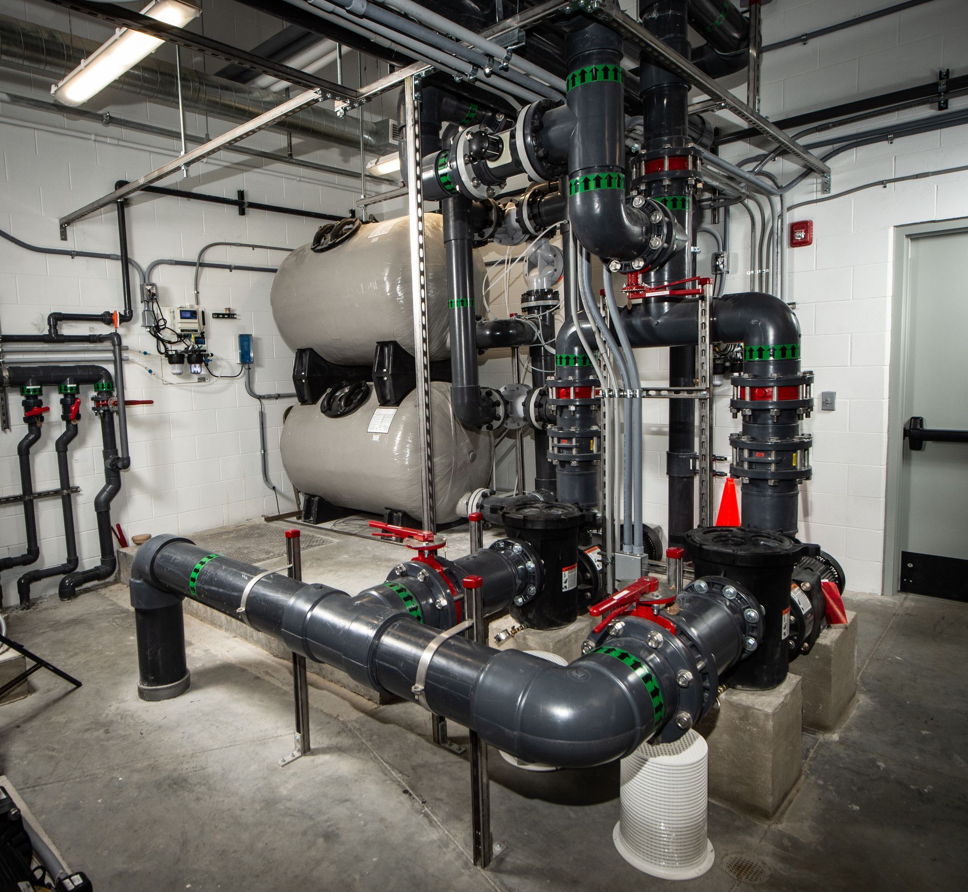 Large industrial piping and tank system in a mechanical room with black pipes, valves, and white pressure tanks.