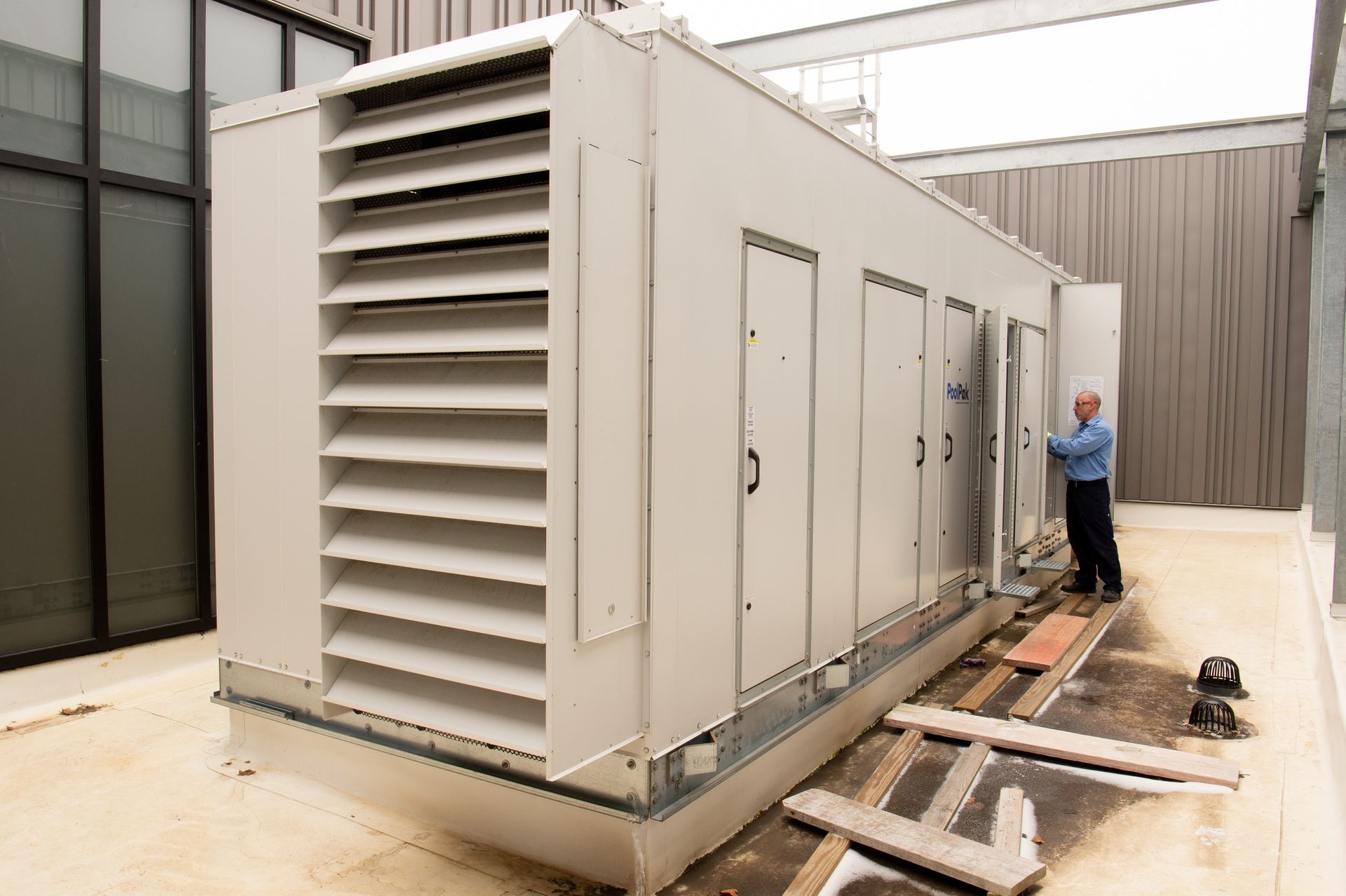 Large white industrial generator unit outdoors beside a building, with a worker inspecting the side panel.