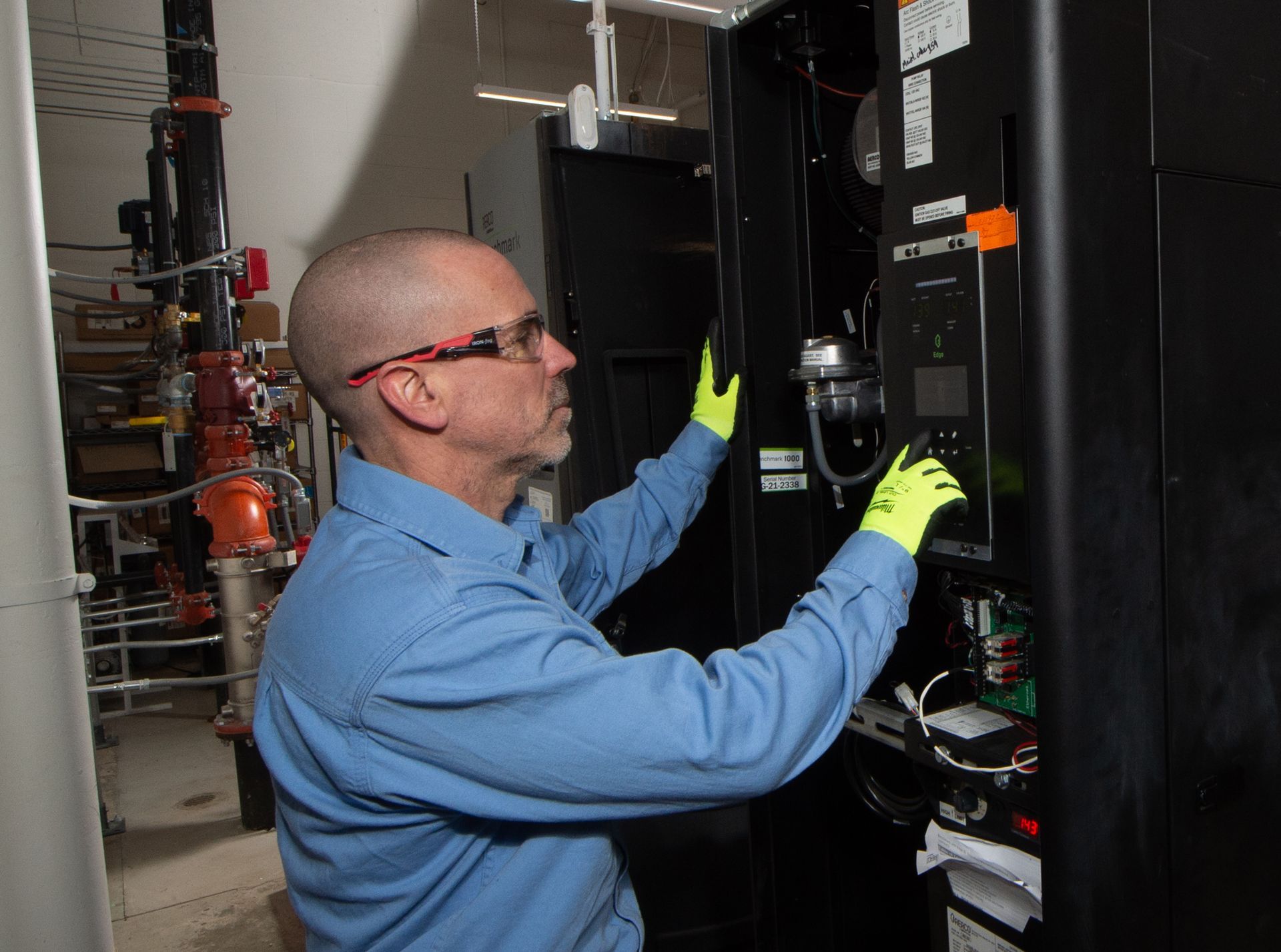 Technician in blue shirt and yellow gloves inspecting a furnace in a utility room