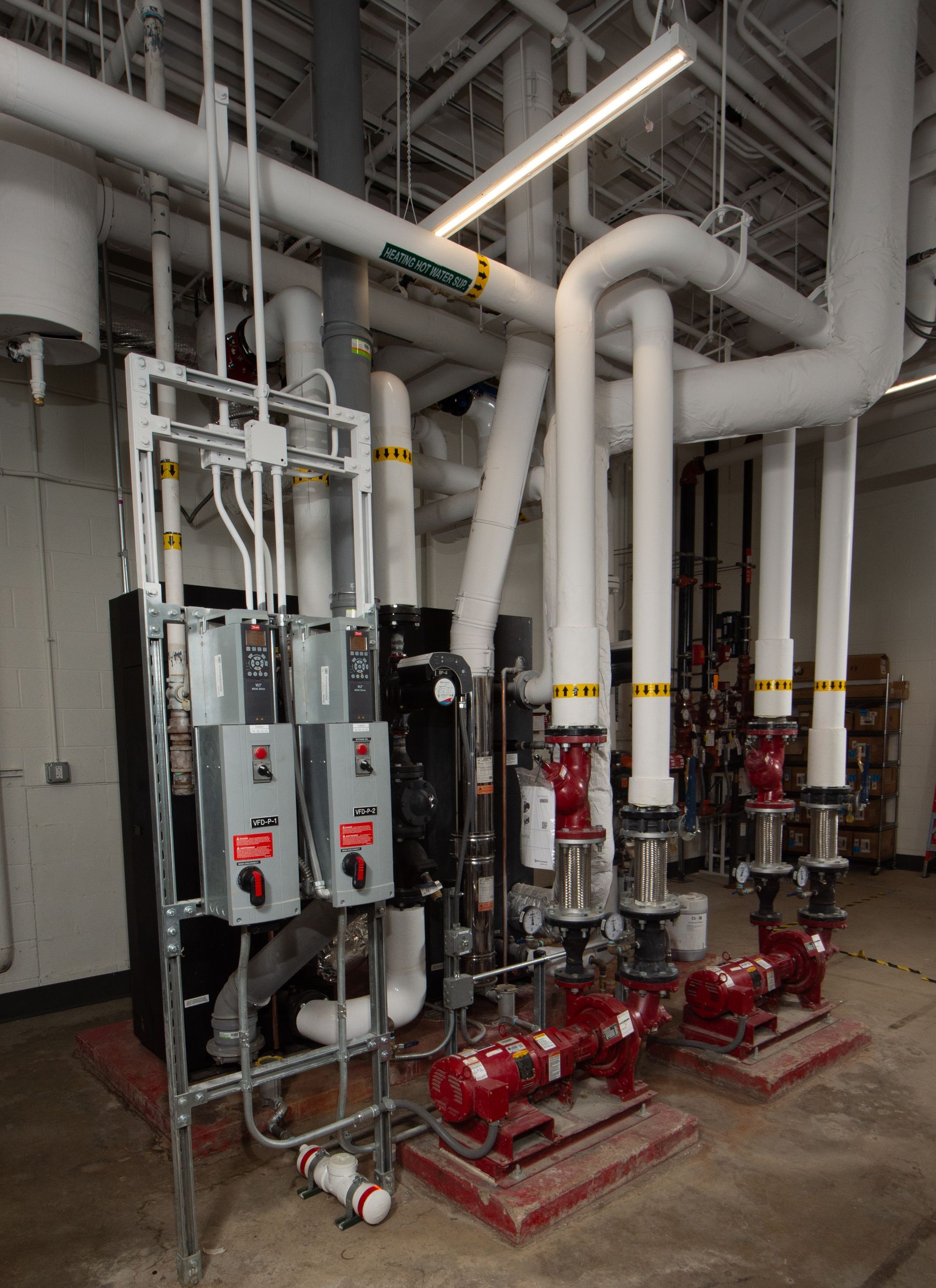 Industrial mechanical room with red pump units, gray control panels, and large white pipes overhead