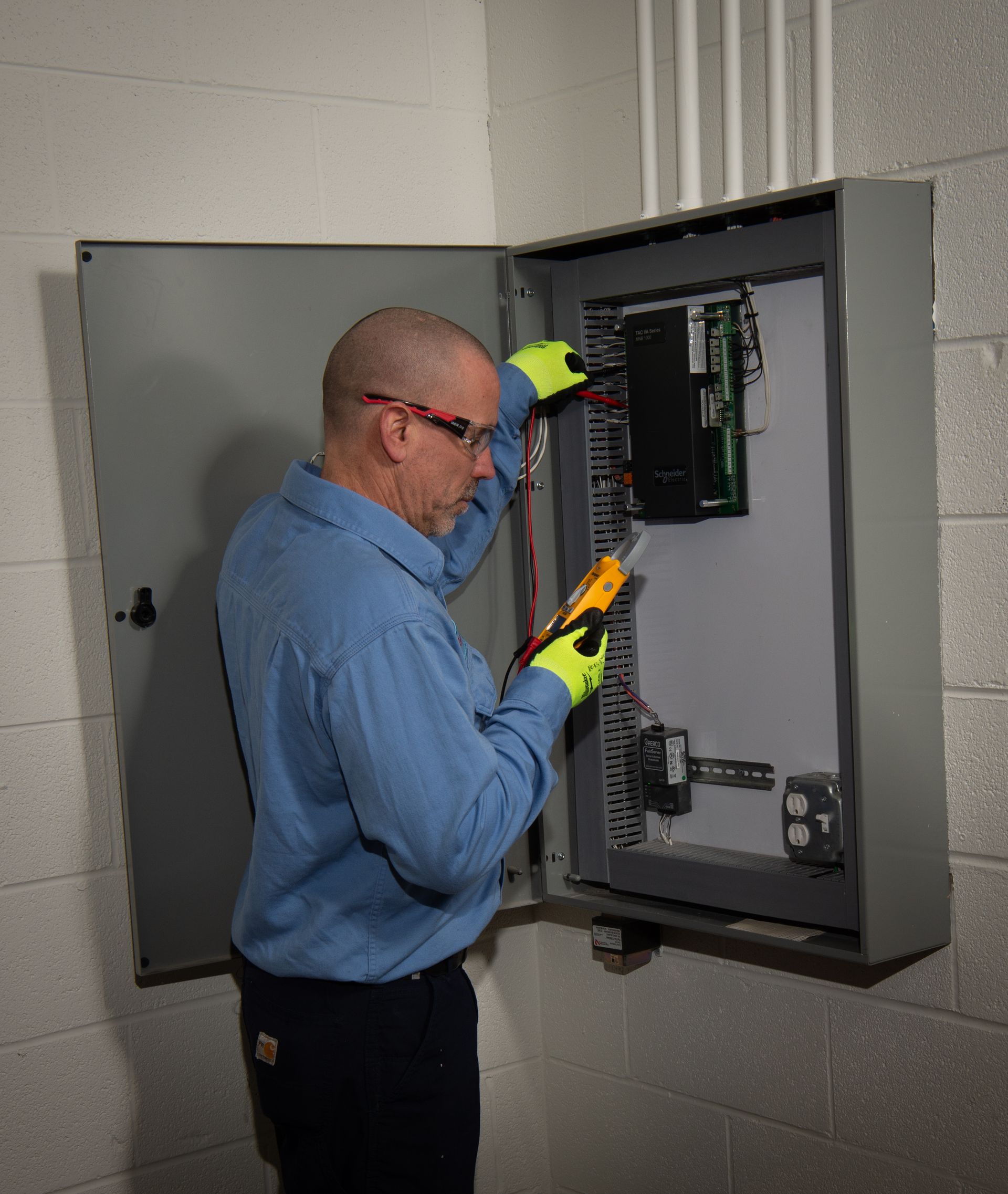 Technician inspecting an open electrical panel while wearing safety gloves and glasses