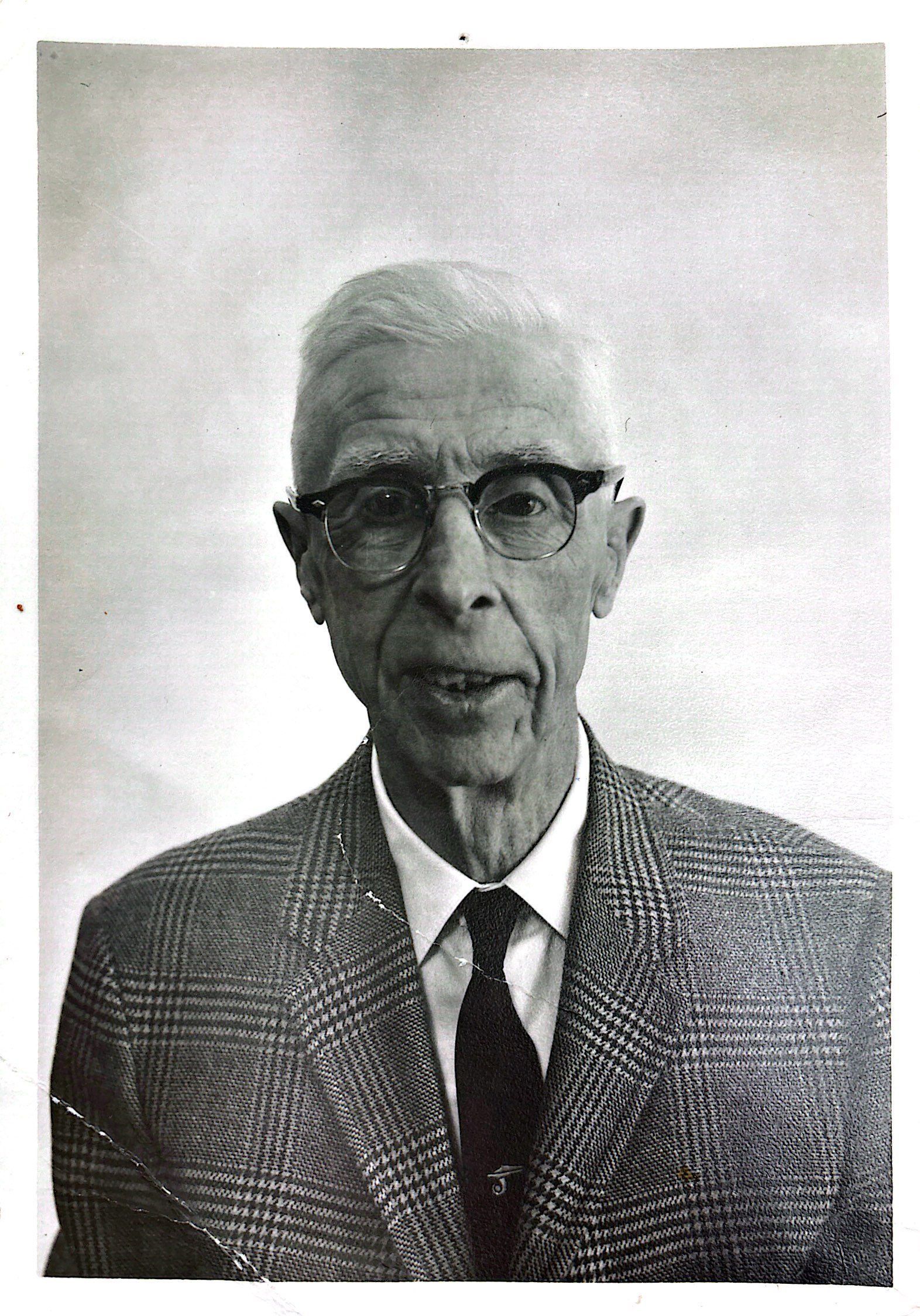 Man wearing glasses, blazer, and tie; looking at the camera.