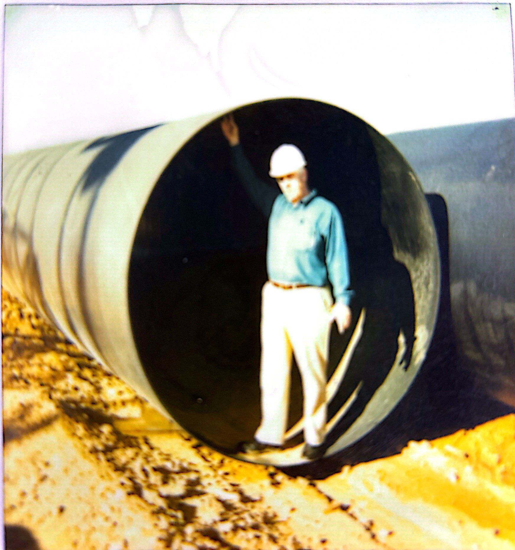 Man standing inside a large pipe, wearing a hard hat, and raising his arm.