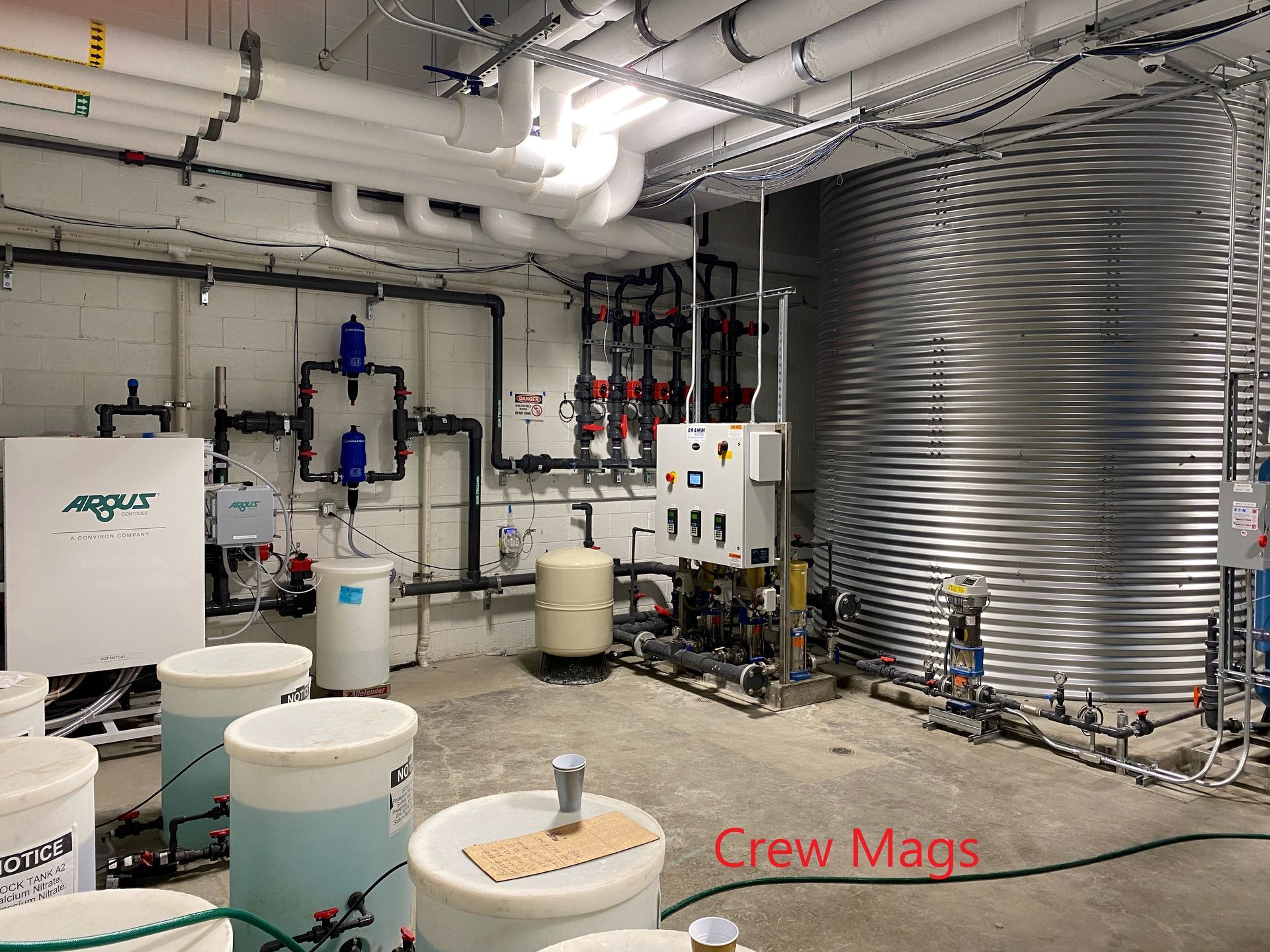 Water treatment facility with tanks, pipes, and control panels in a concrete room.