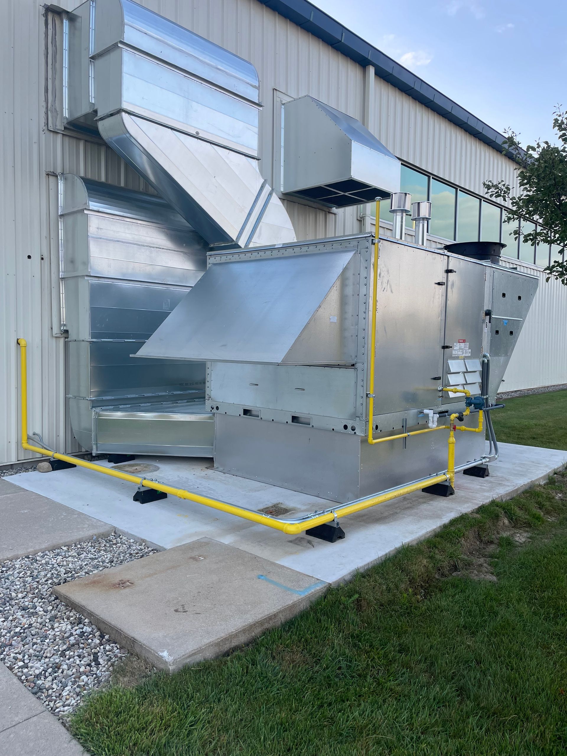 Exterior heat pump unit on a concrete pad near a house with blue siding and rock landscaping.