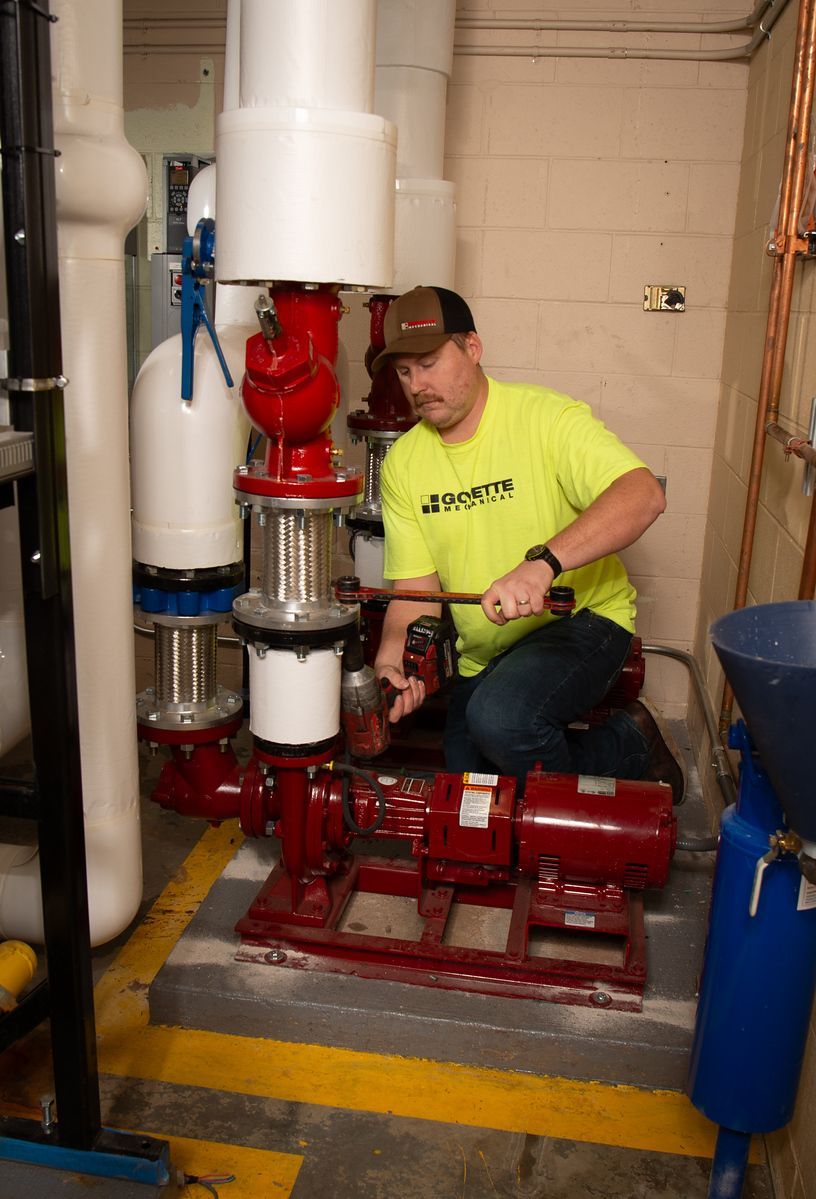 Man in yellow shirt repairs red pump in an industrial setting.
