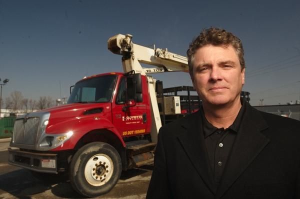 Man standing in front of a red utility truck with an extended crane against a blue sky.