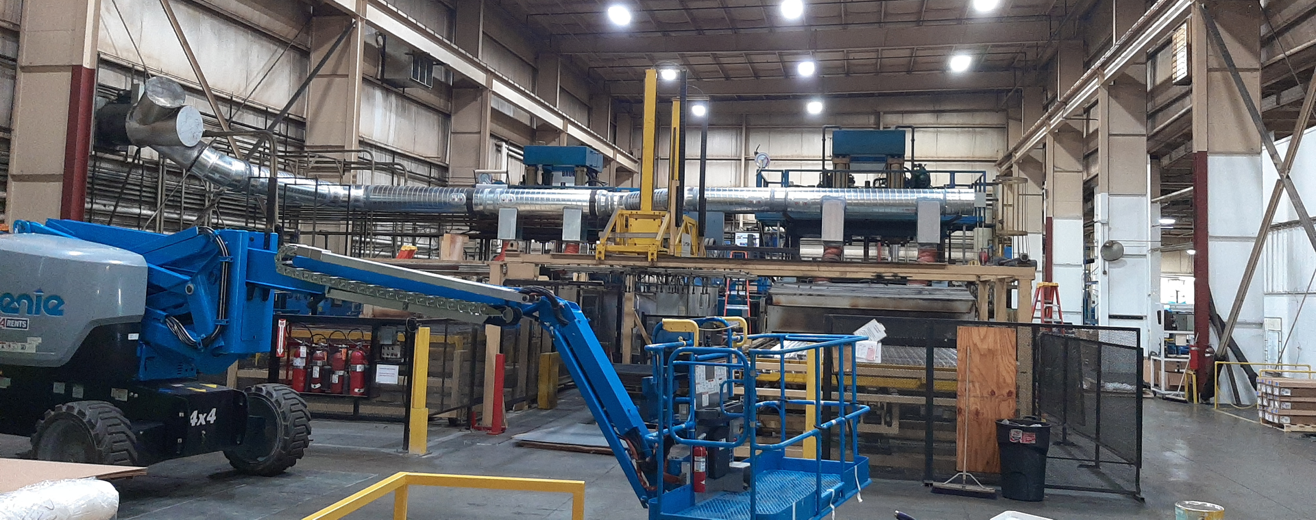 A large factory interior with blue lift equipment, ductwork, and machinery.
