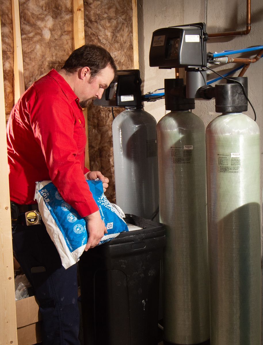 Man in red shirt filling a salt tank for a water softener system.