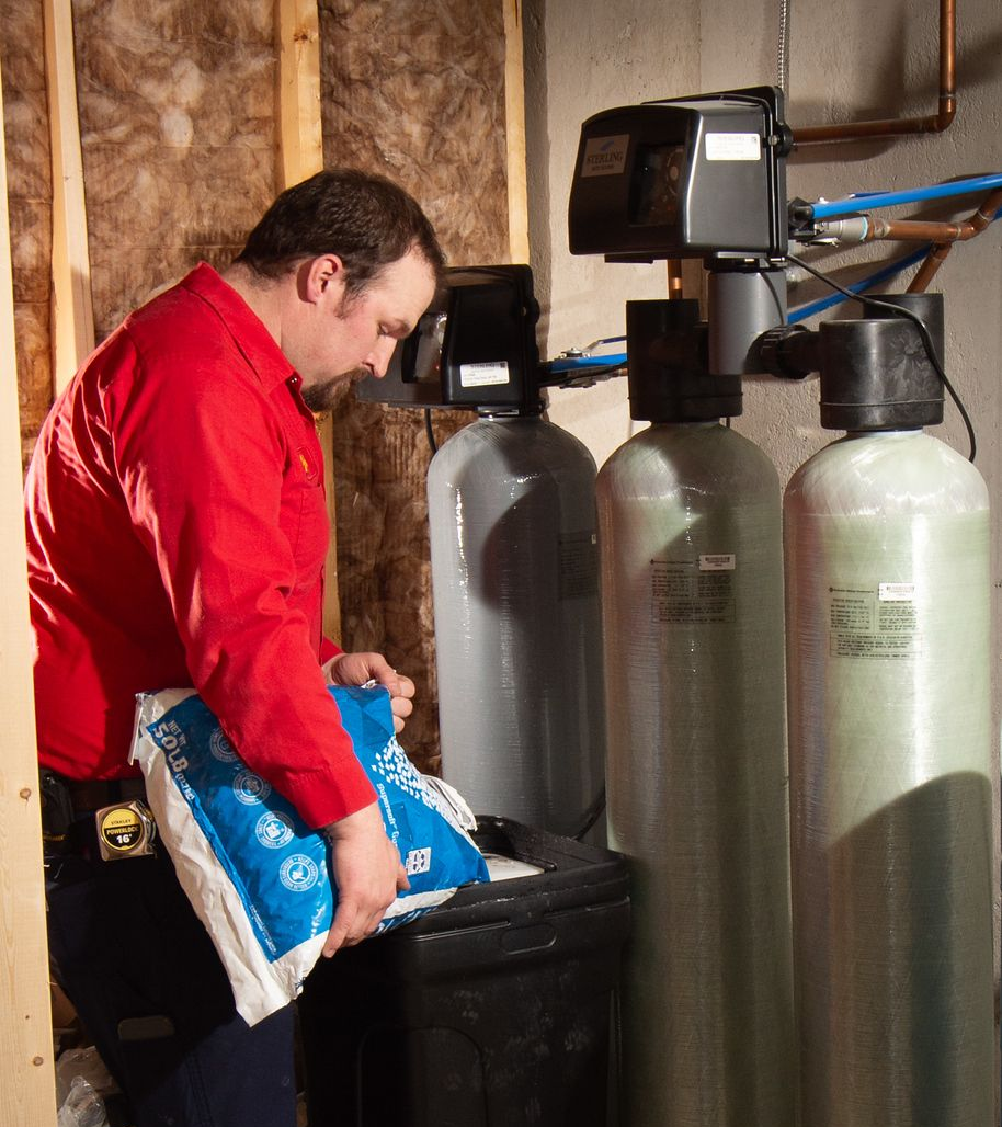 Man in red shirt filling a salt tank for a water softener system in a basement.