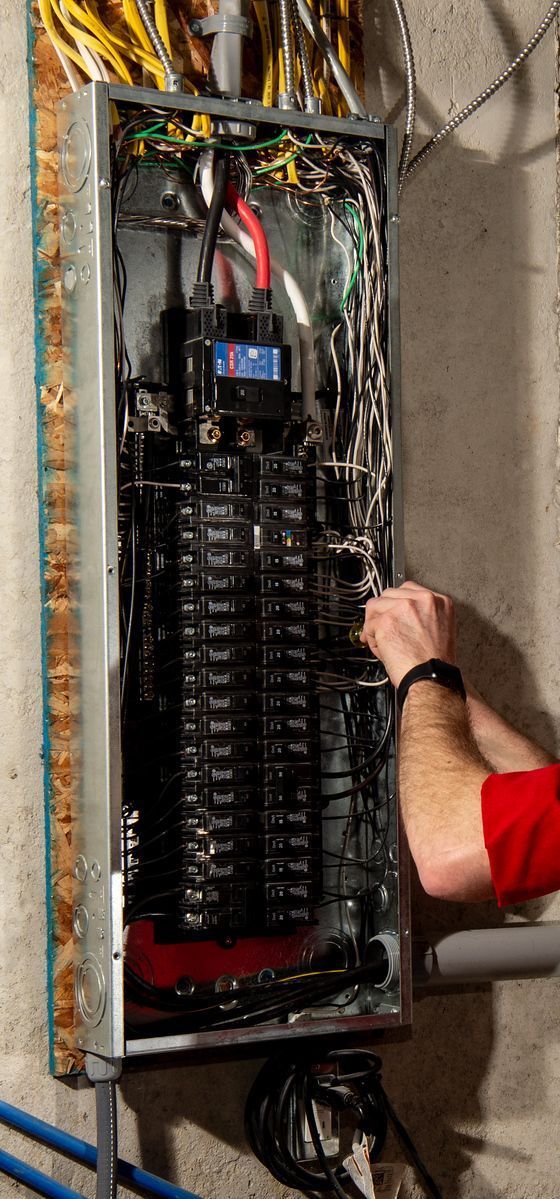 Open electrical breaker panel with exposed wiring; person in red shirt is working inside.
