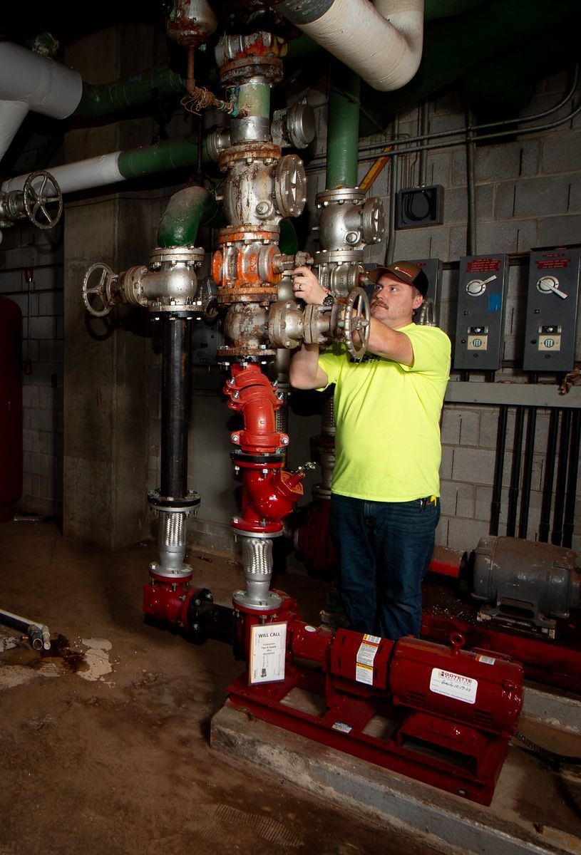 Man in safety vest working on industrial pipes in a utility room.