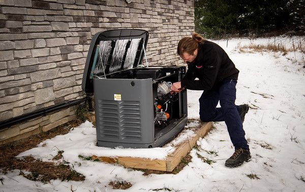 Person inspecting an outdoor generator beside a brick building in the snow