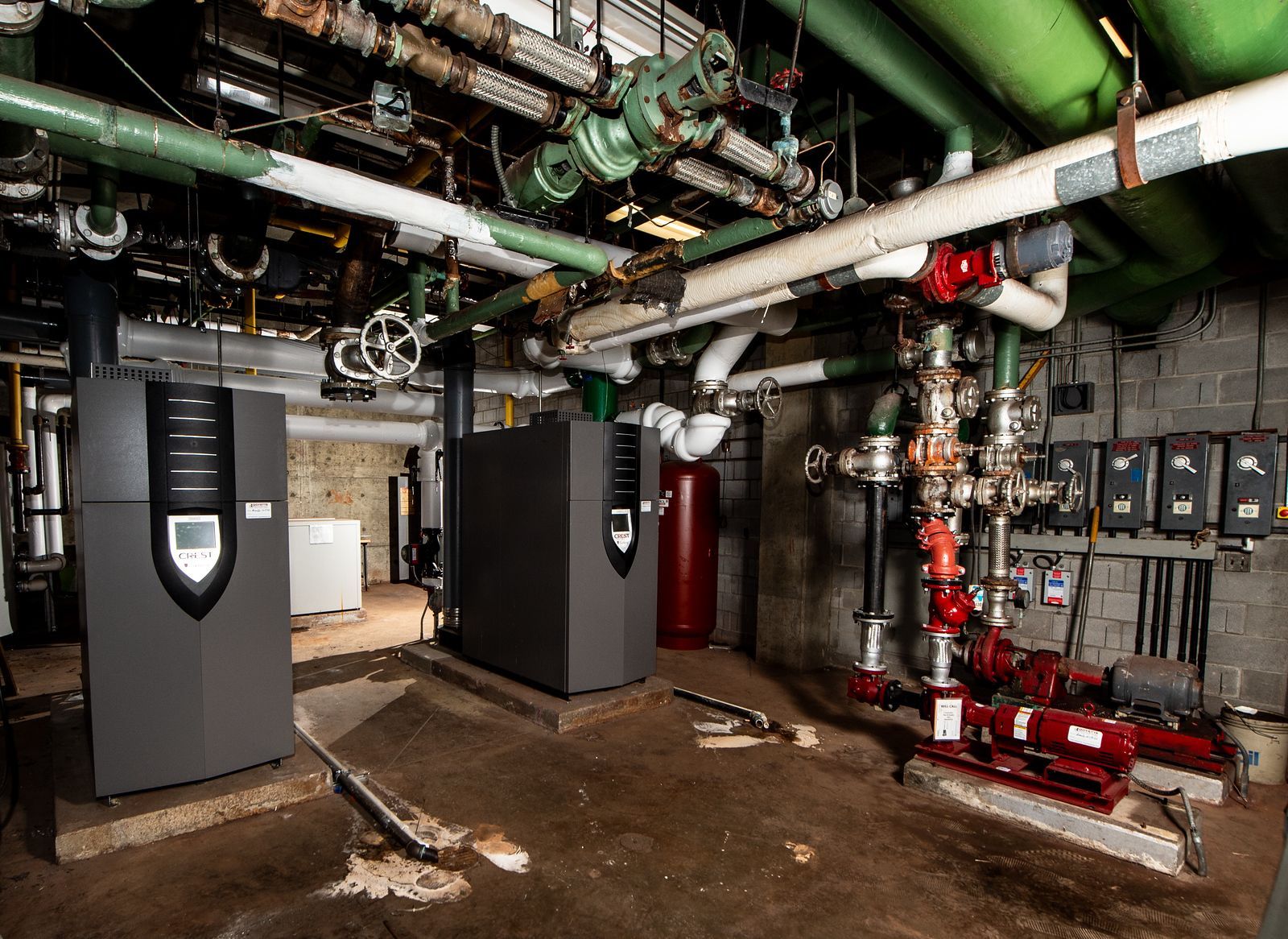Two grey heating units in a utility room with pipes and valves.