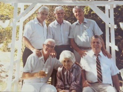 Six people pose for a photo in front of a white gazebo. The woman is seated, the men are standing or sitting.
